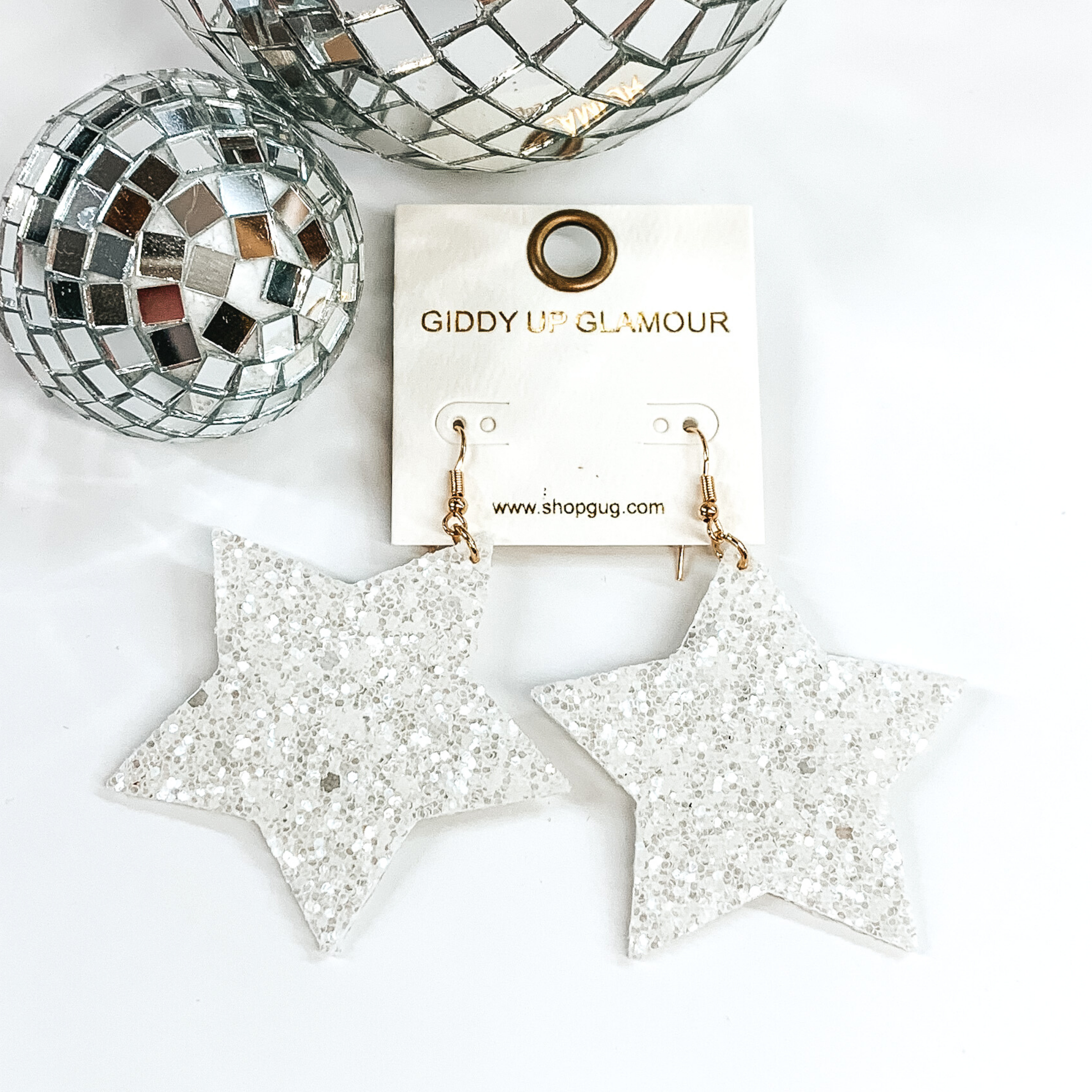 Glitter star dangle earrings in white with a gold earrings hook. These earrings are pictured on a white background with a disco ball at the top of the picture.