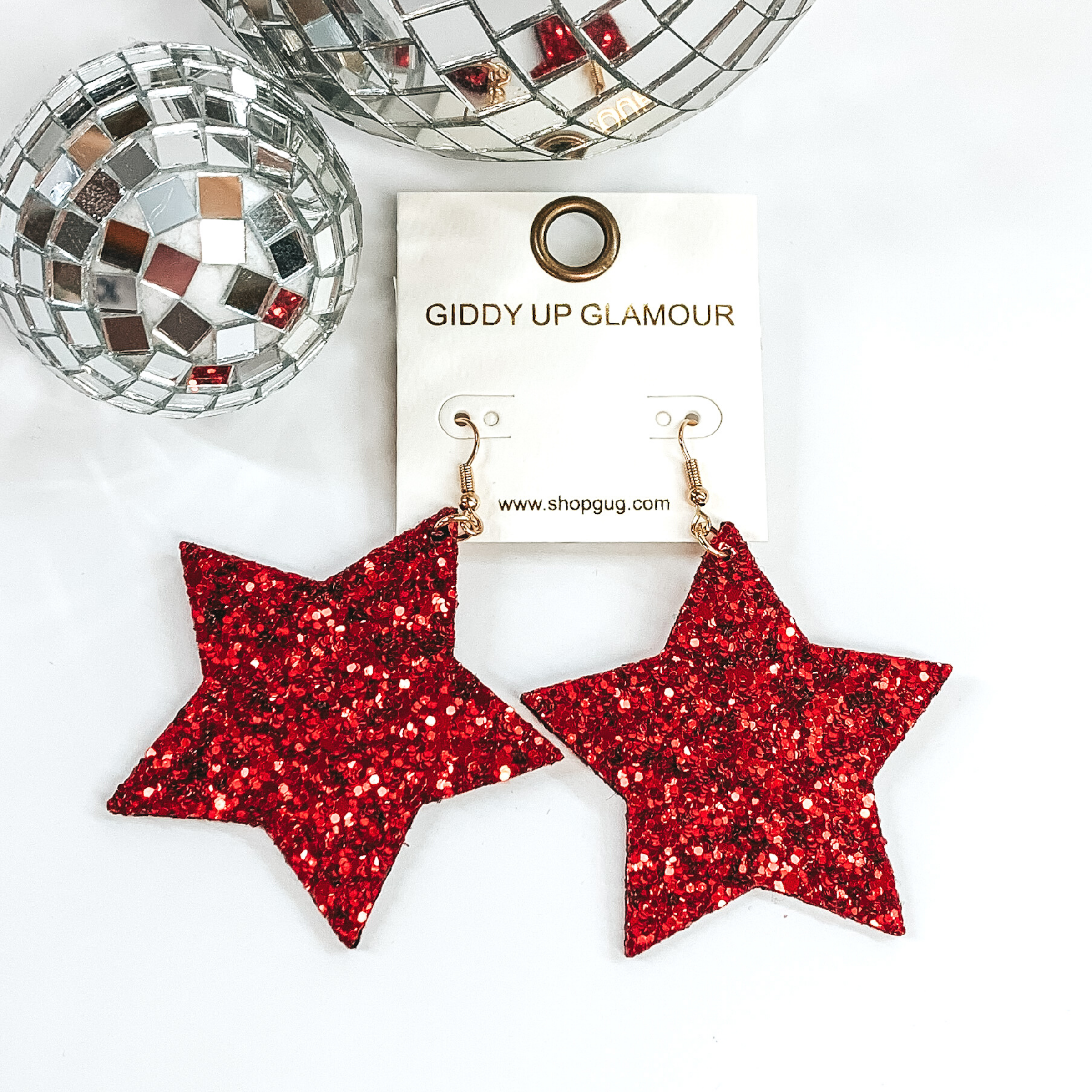 Glitter star dangle earrings in red with a gold earrings hook. These earrings are pictured on a white background with a disco ball at the top of the picture.
