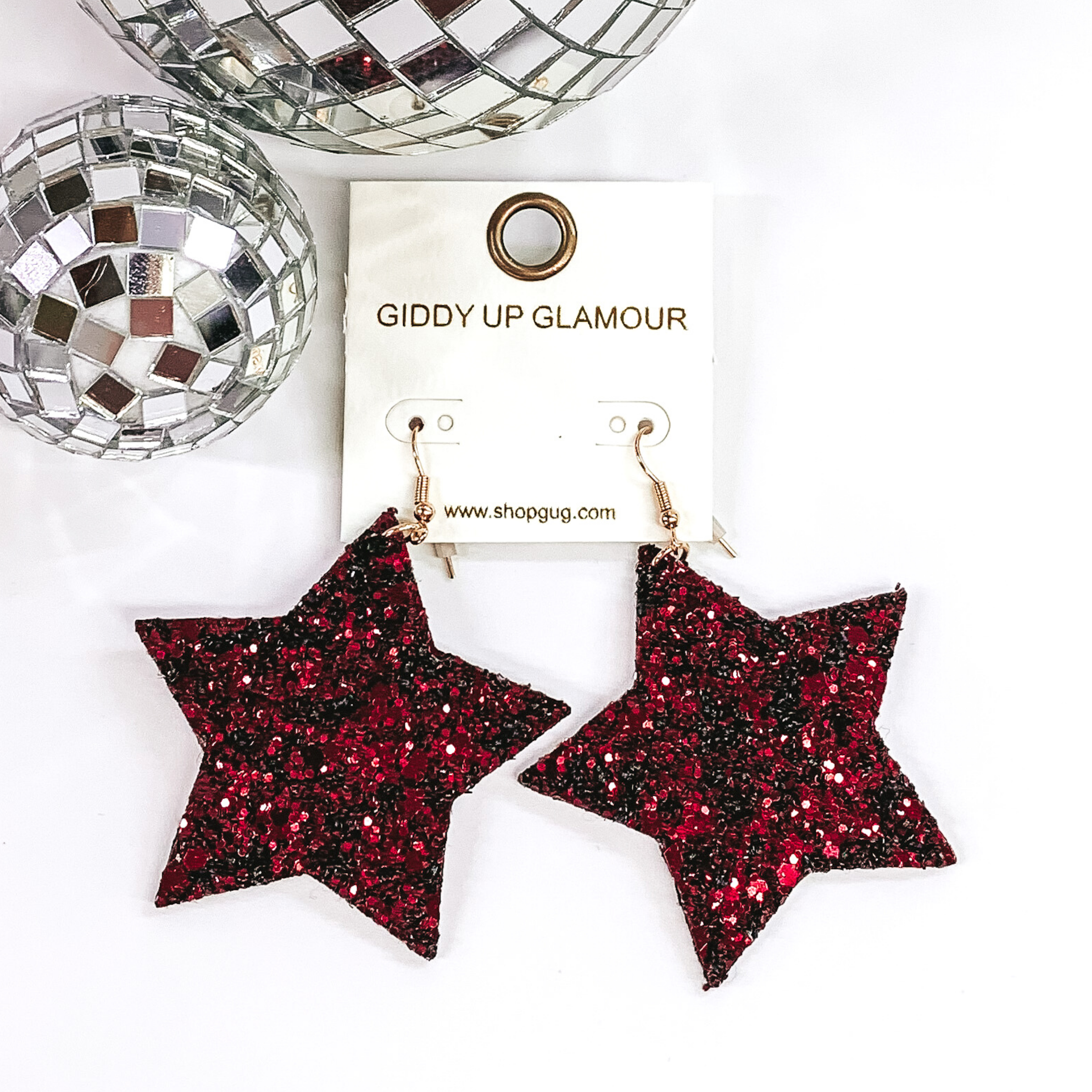 Glitter star dangle earrings in burgundy with a gold earrings hook. These earrings are pictured on a white background with a disco ball at the top of the picture.