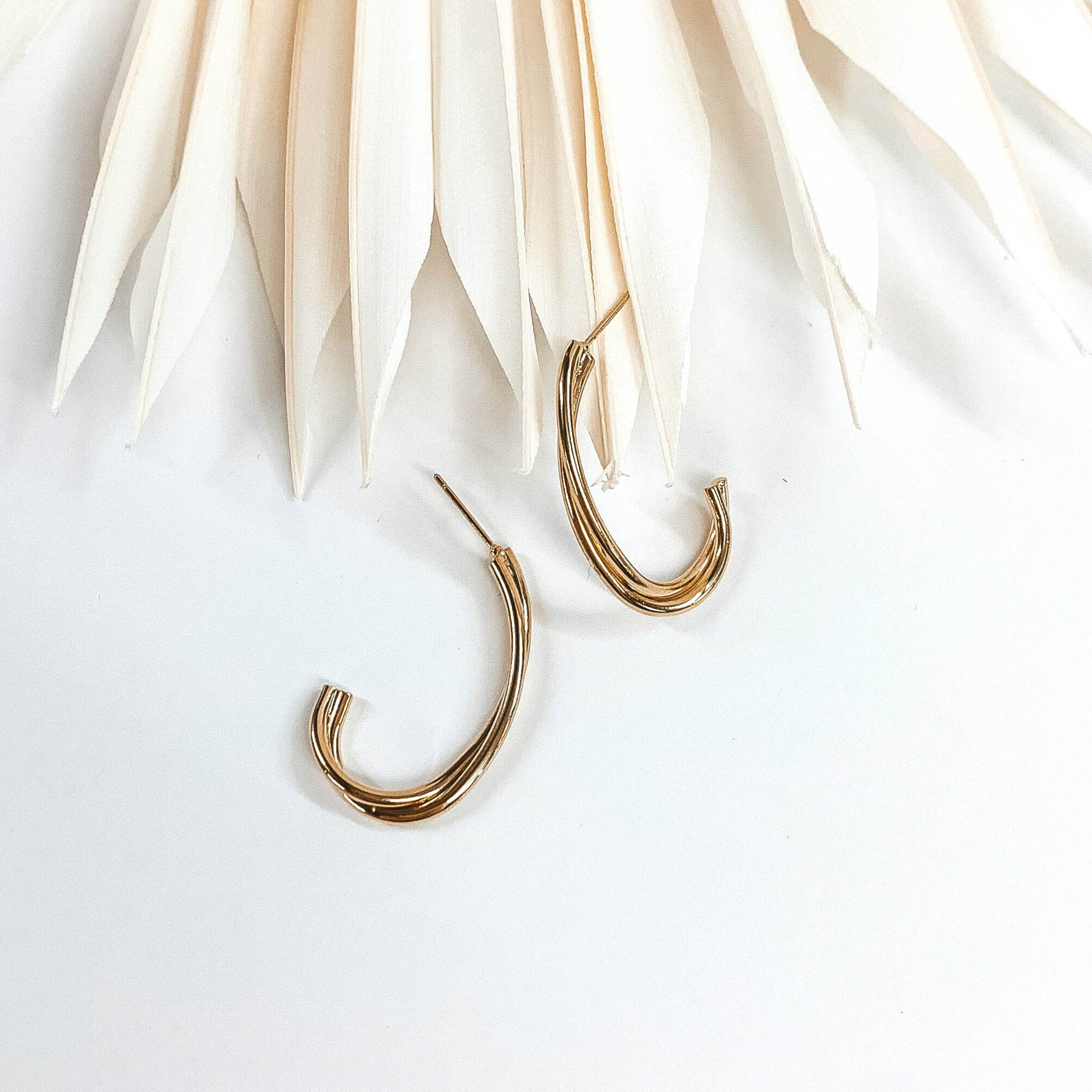 Gold twisted oval hoops with two layers. These earrings are pictured on a white earrings holder laying on white blocks.