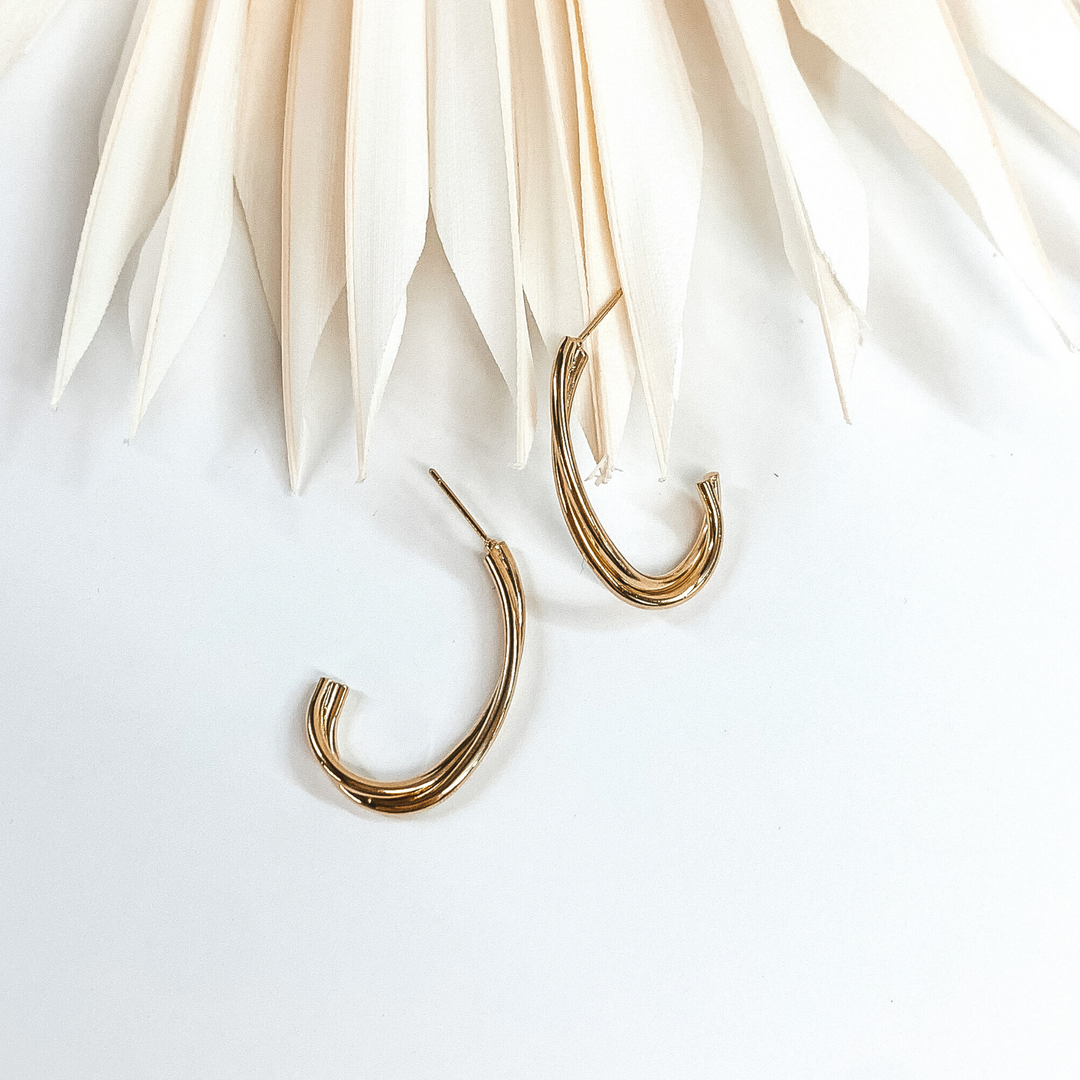 Gold twisted oval hoops with two layers. These earrings are pictured on a white earrings holder laying on white blocks.