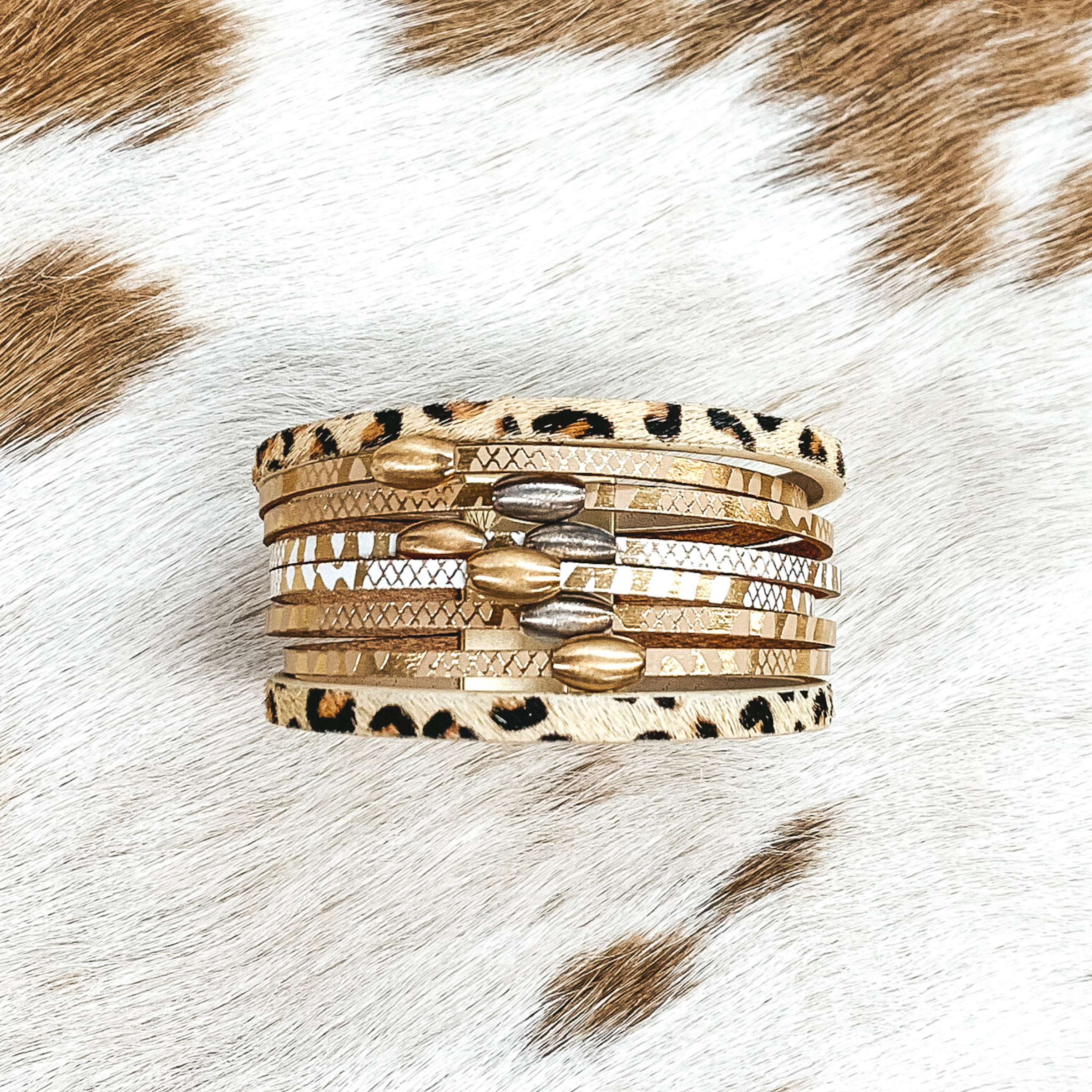 Animal print strands that include silver and gold beads. This bracelet is pictured on a white and brown cow print background. 