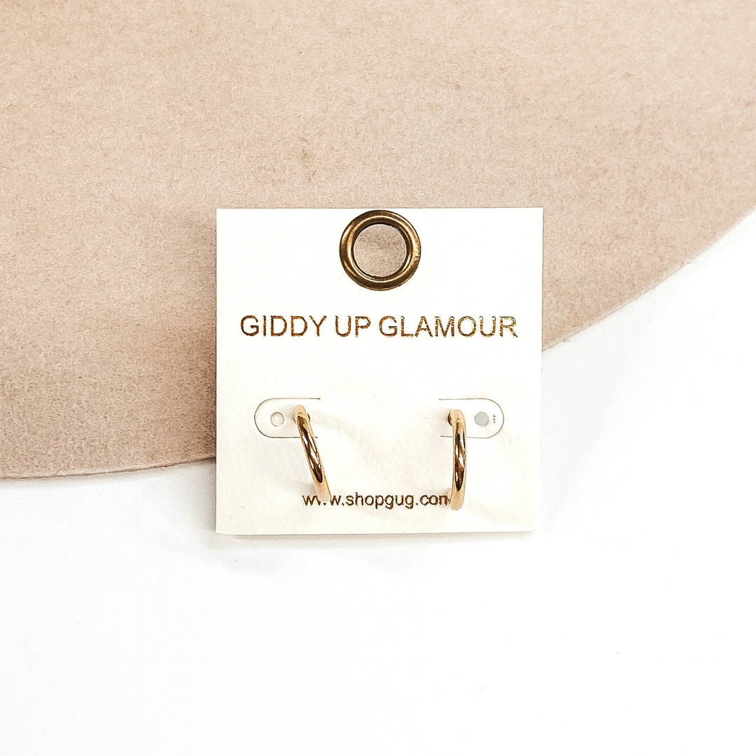 Thin gold hoops on a white earrings holder. These hoops are pictured on a white and beige background.