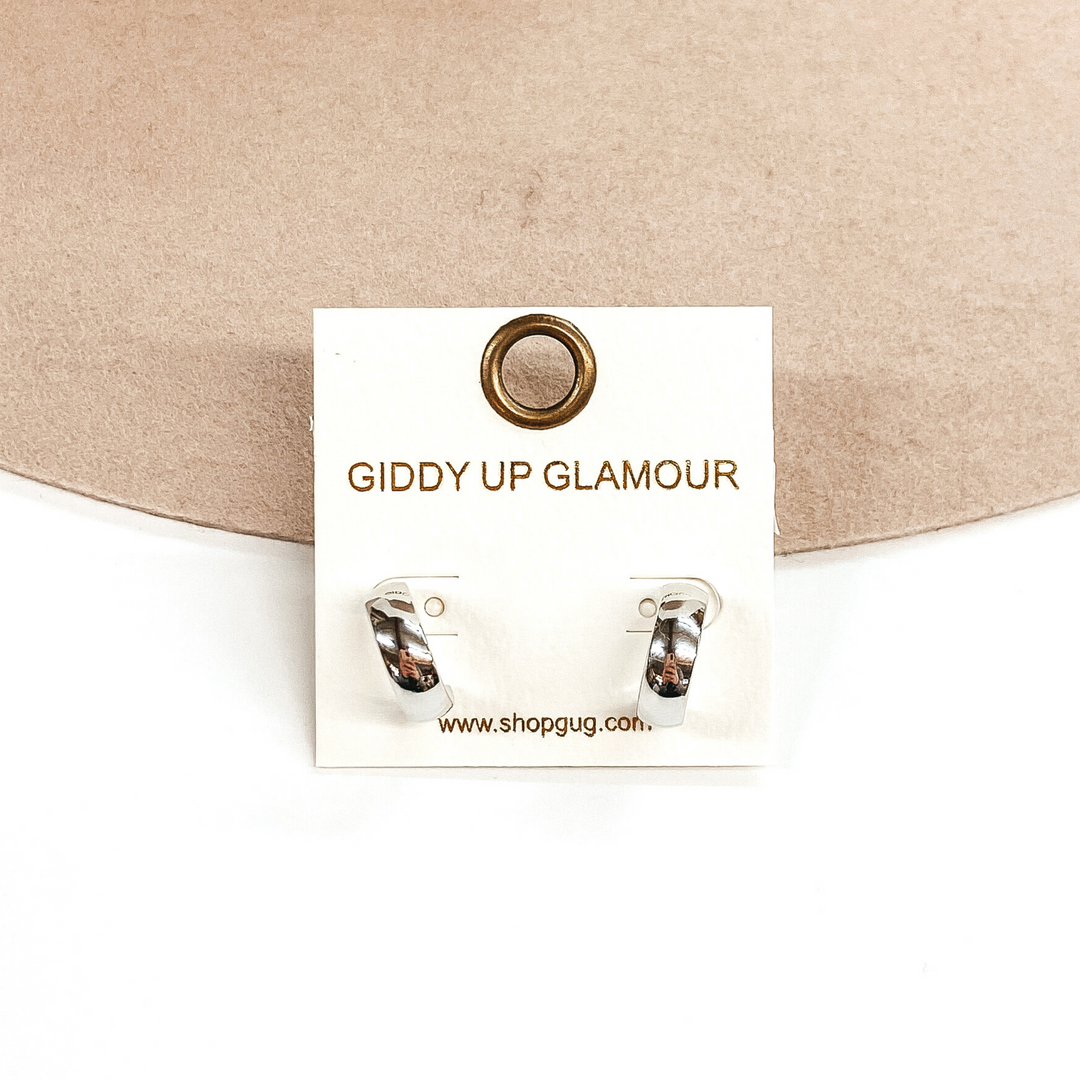 Silver curved hoops pictured on a white earrings holder. These hoops are pictured on a white and beige background. 