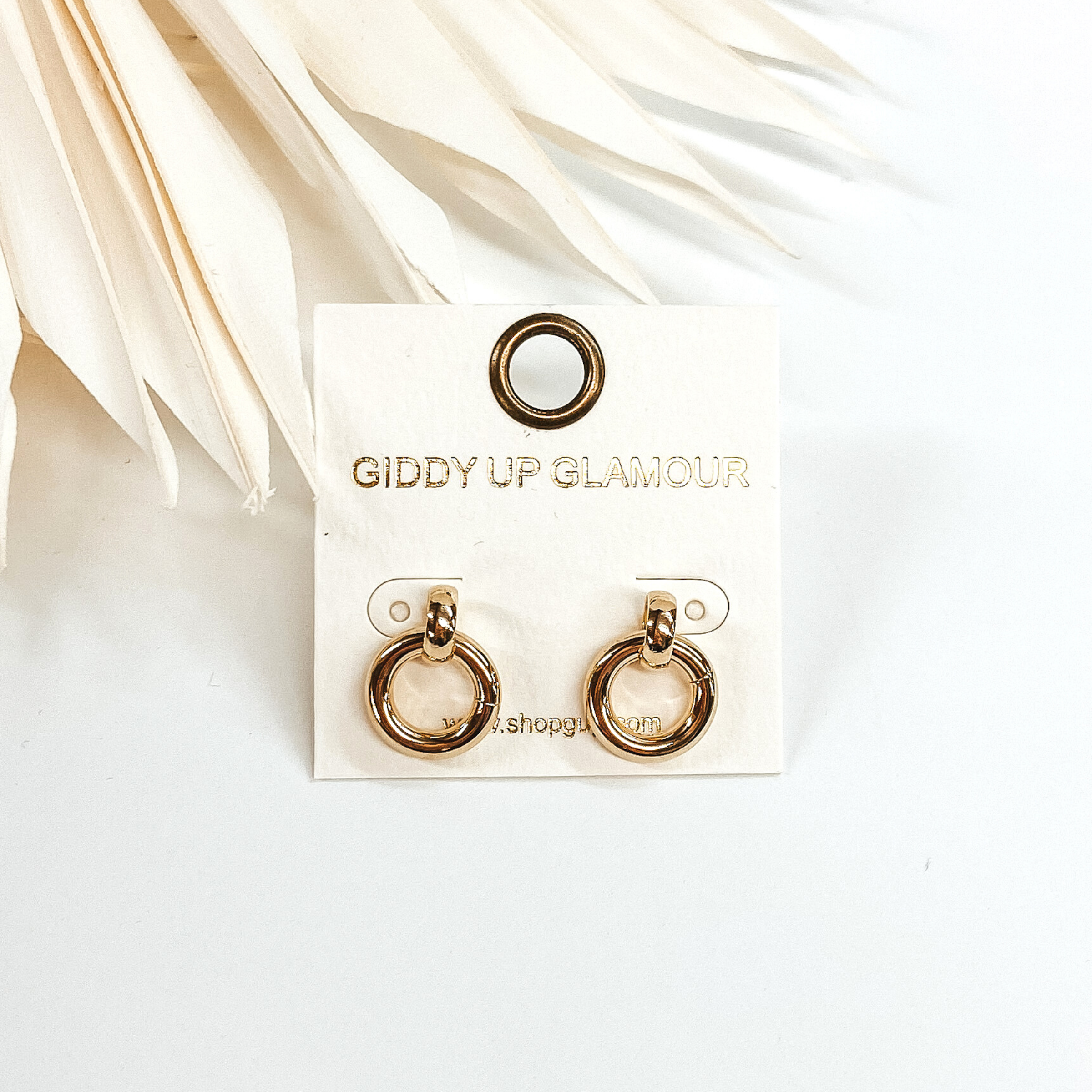 Tiny circle drop earrings in gold. These earrings are pictured in front of white leaves and on a white background.