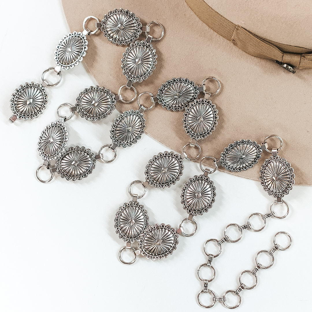 Classic silver concho belt with silver circle loops to make it adjustable. This belt is pictured partially laying on a beige colored hat on a white background. 