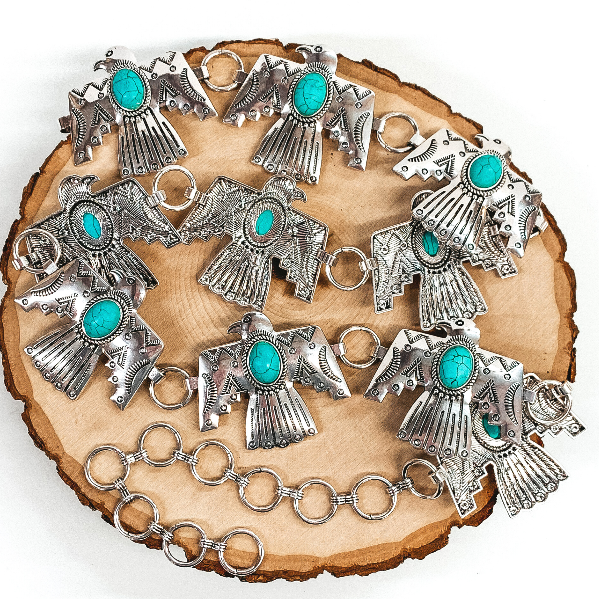 Silver thunderbird belt with center oval turquoise stones. This belt has circle loops to make it adjustable. This belt is pictured on a piece of wood on a white background. 