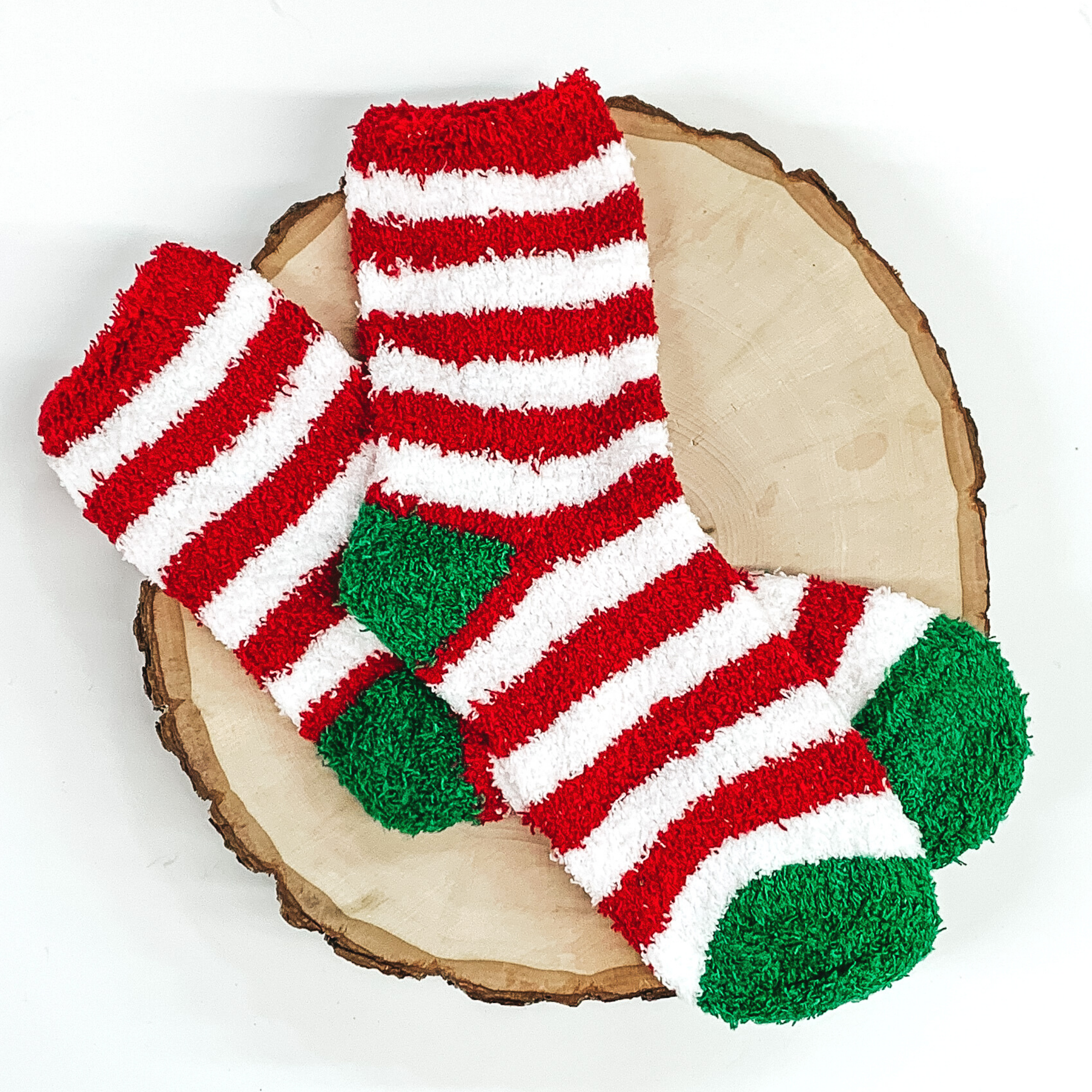 Fuzzy red and white striped socks with green toes and heels. These socks are pictured laying on a piece of wood that is on a white background.