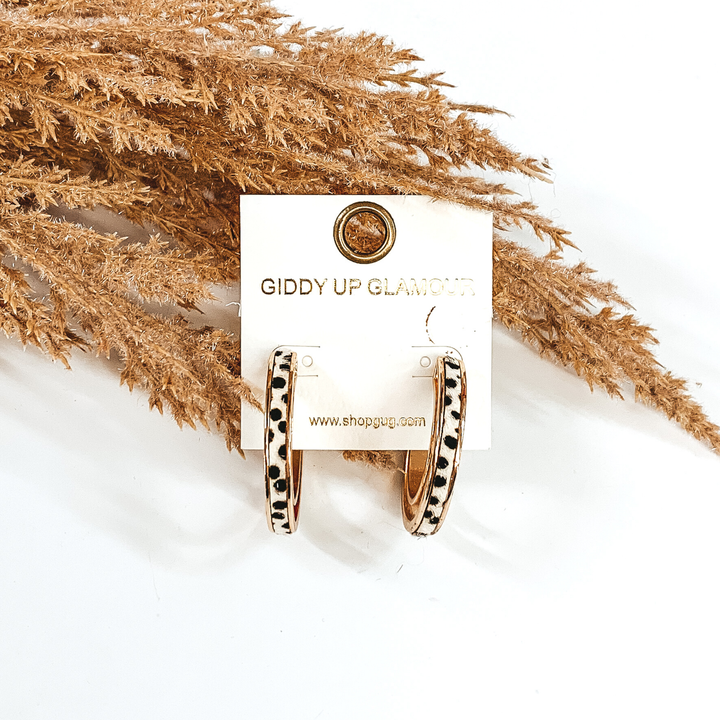 Gold hoops with white dotted print inlay. these hoop are pictured on a white background and in front of some tan floral.