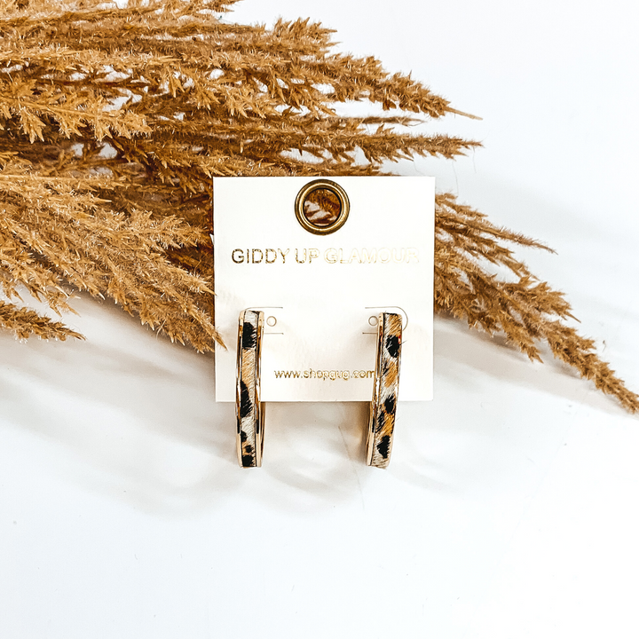 Gold hoops with white animal print inlay. these hoop are pictured on a white background and in front of some tan floral.