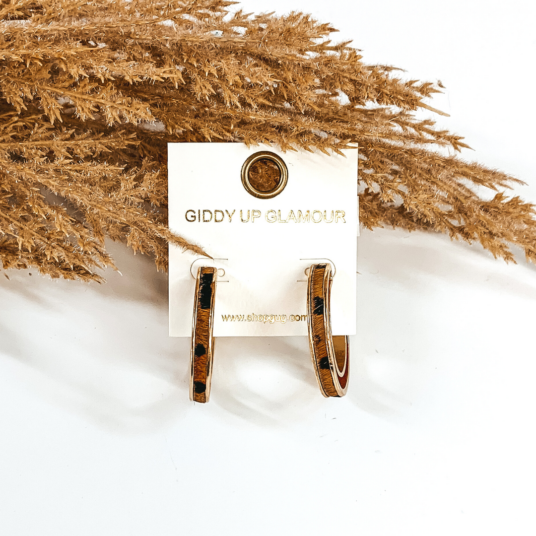 Gold hoops with brown animal print inlay. these hoop are pictured on a white background and in front of some tan floral. 