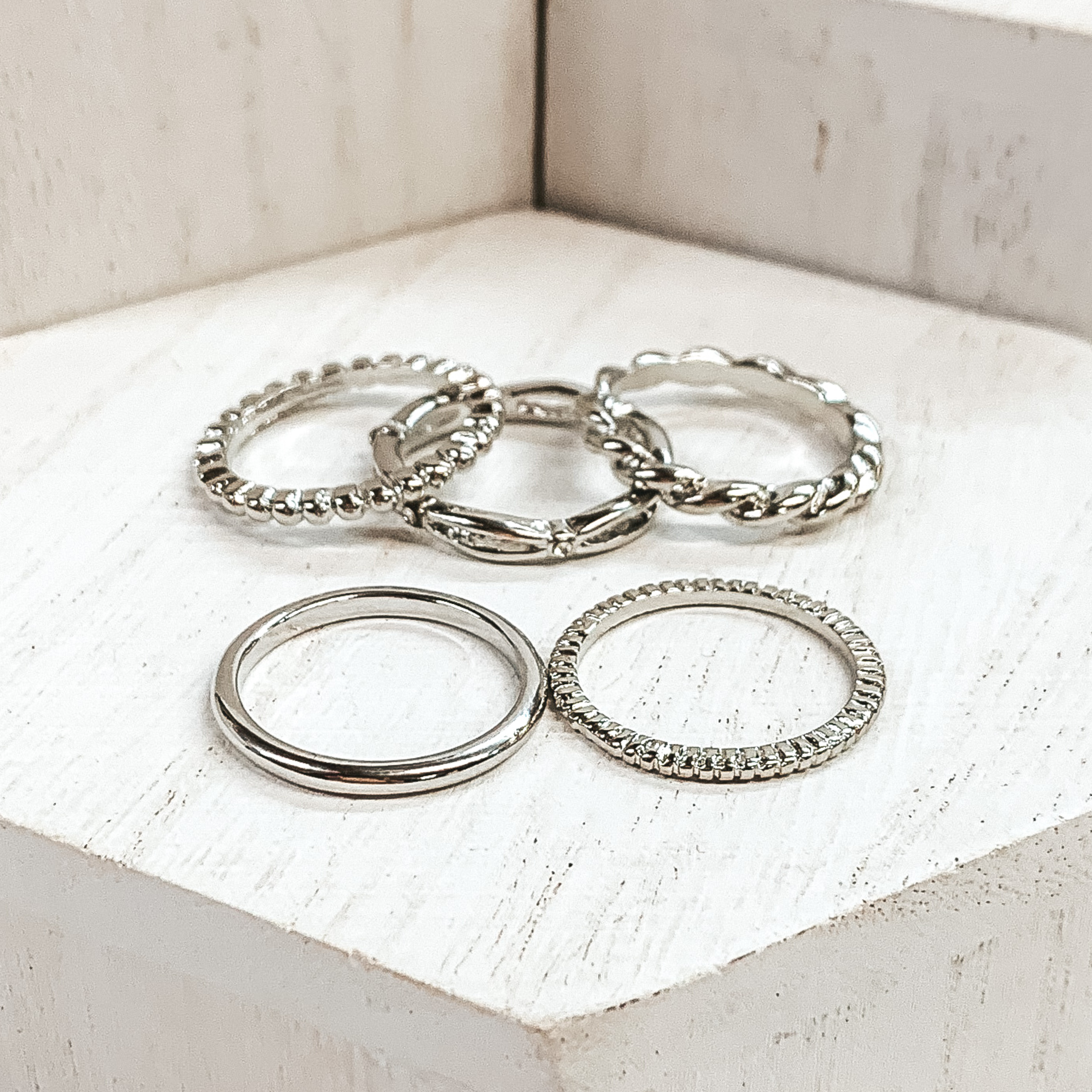 Set of five silver rings. One is a plain band, one is a bubble band, one is a twisted band, and the other two are textured bands. These rings are pictured on white blocks.
