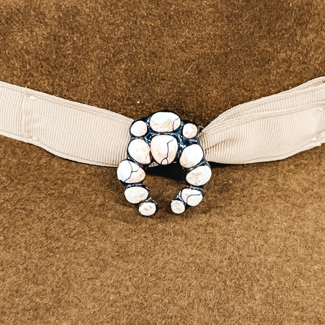 This hat pin is a small squash blossom. The main color is ivory and is mixed with brown like real white buffalo. This hat pin is pictured in front of a beige hat band.