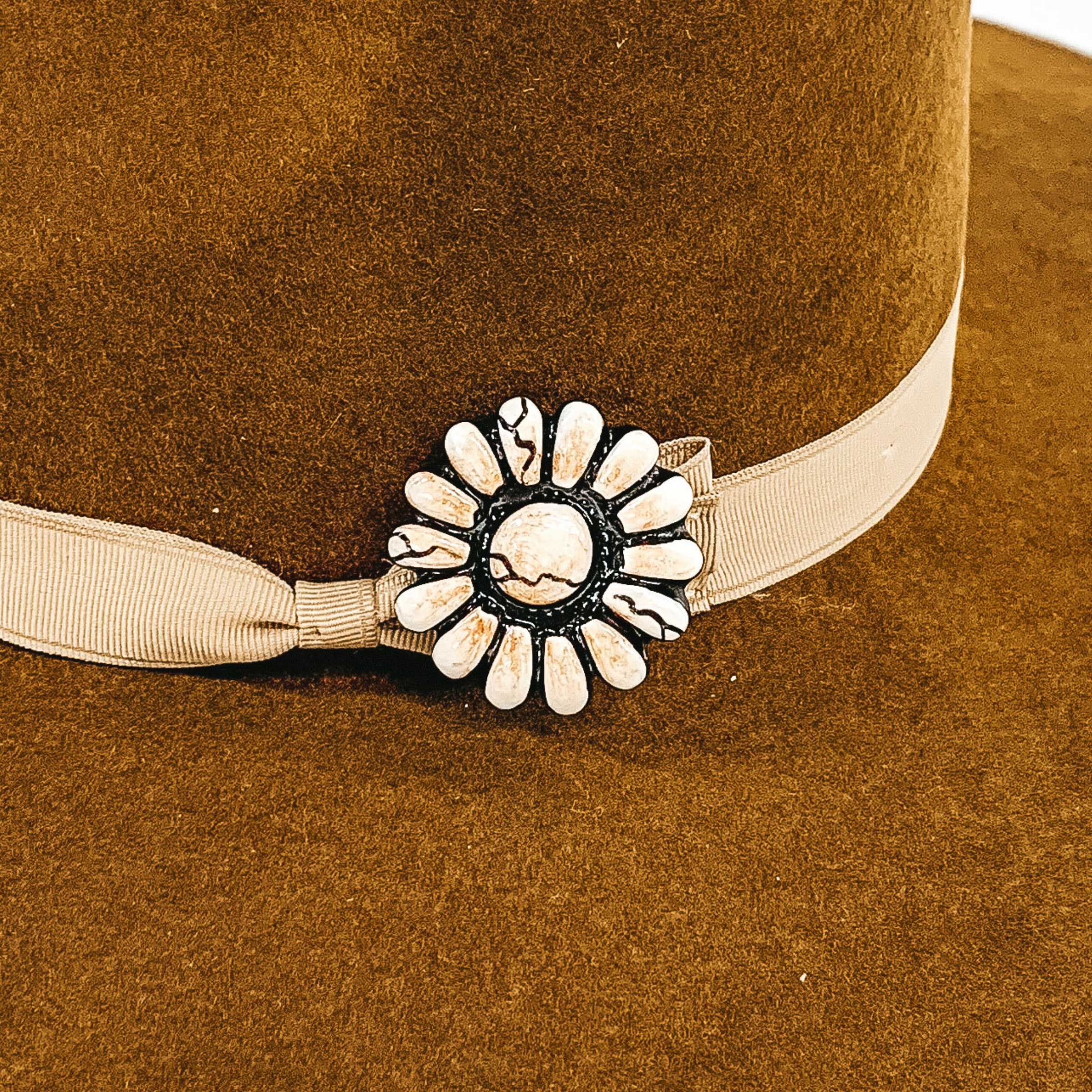 This hat pin is a flower concho. The main color is ivory and is mixed with brown like real white buffalo. This hat pin is pictured in front of a beige hat band.