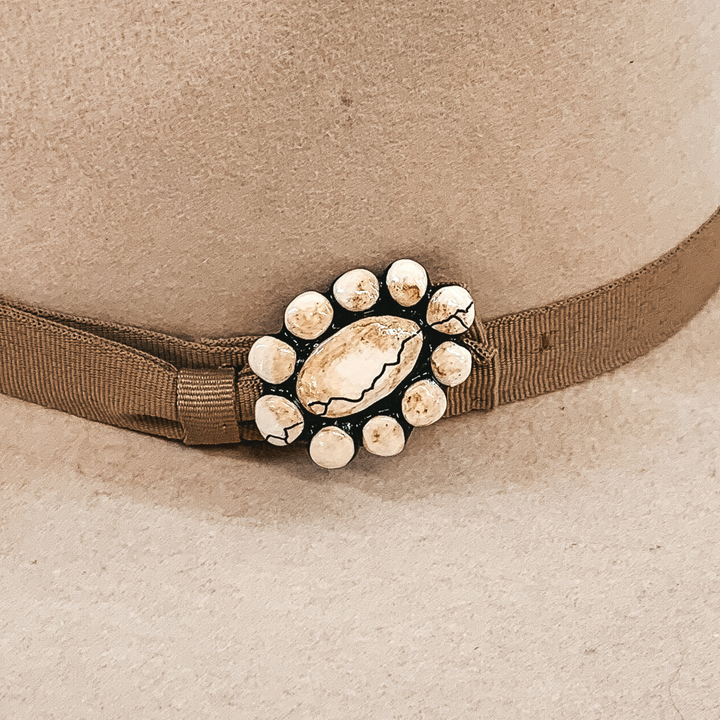 This hat pin is a short, oval concho. The main color is ivory and is mixed with brown like real white buffalo. This hat pin is pictured in front of a beige hat band.