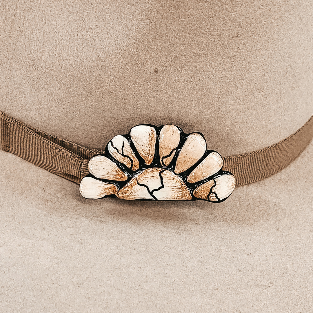 This hat pin is a half of a concho. The main color is ivory and is mixed with brown like real white buffalo. This hat pin is pictured in front of a beige hat band.