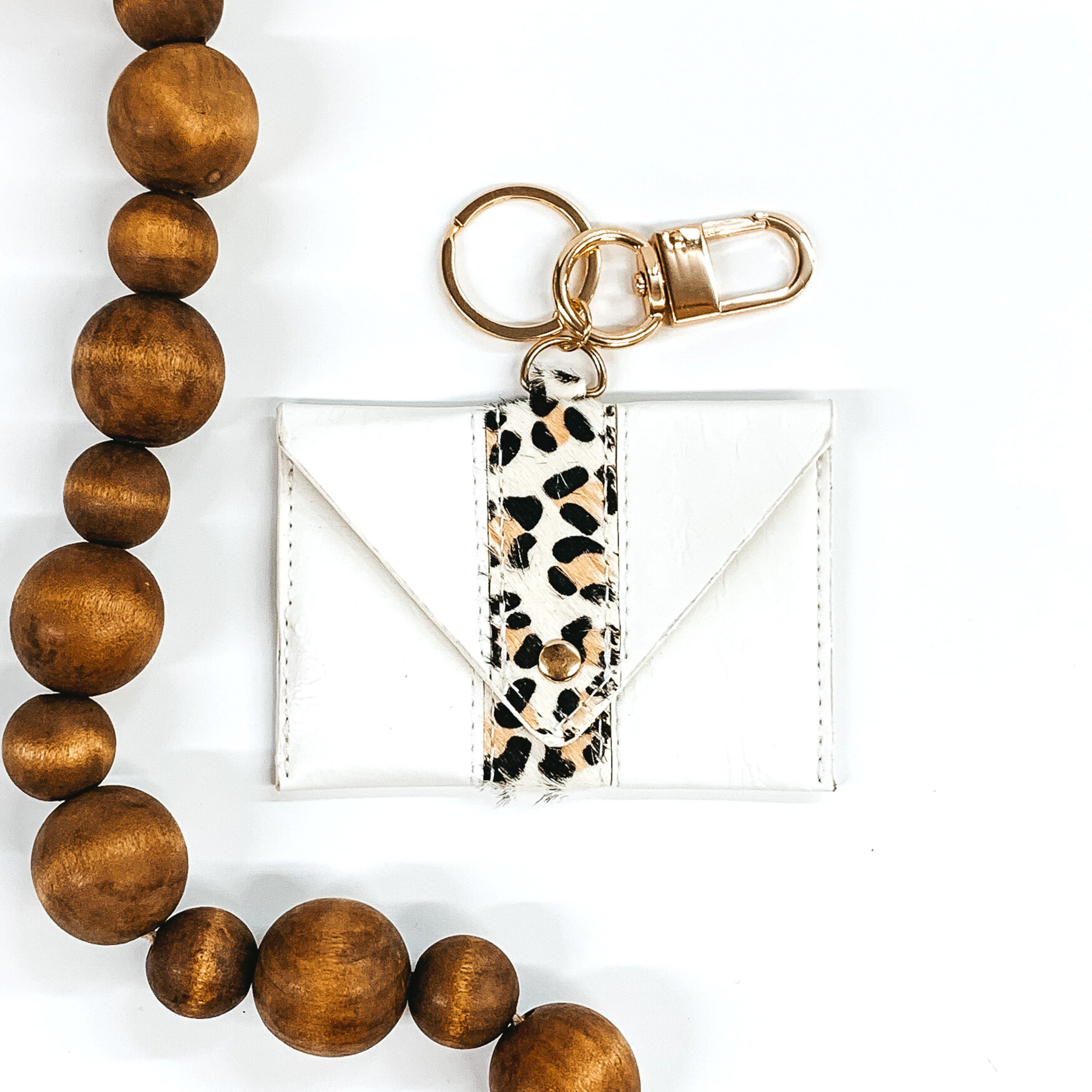 White leather rectangle wallet with hair on hide leopard stripe and snap closure that includes a gold key ring. This keychain is pictured on a white background with brown beads on the  left side. 