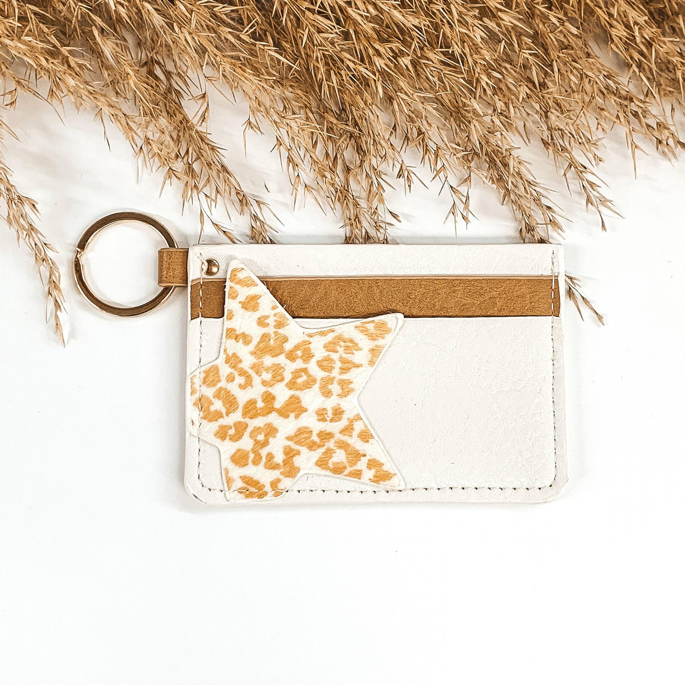 This is a rectangle id key holder that has a gold key ring. On the front you have ivory and tan layer and then a white star with a tan leopard print is also on the front. It is pictured on a a white background that has brown floral at the top of the picture.