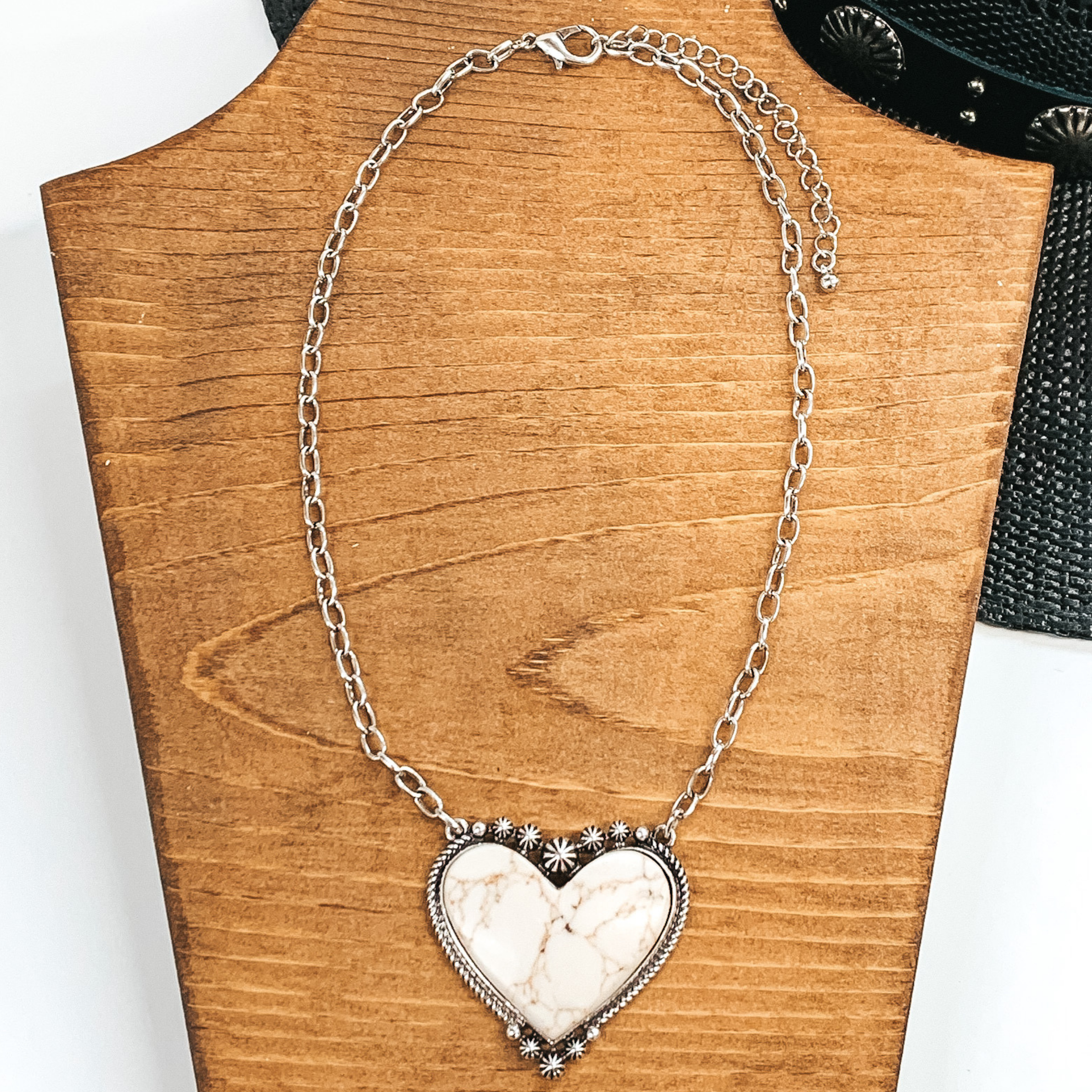 Silver chained necklace with heart pendant. The heart pendant is outlined in silver with an ivory stone. This necklace is pictured on a wood necklace holder on a white and black background.