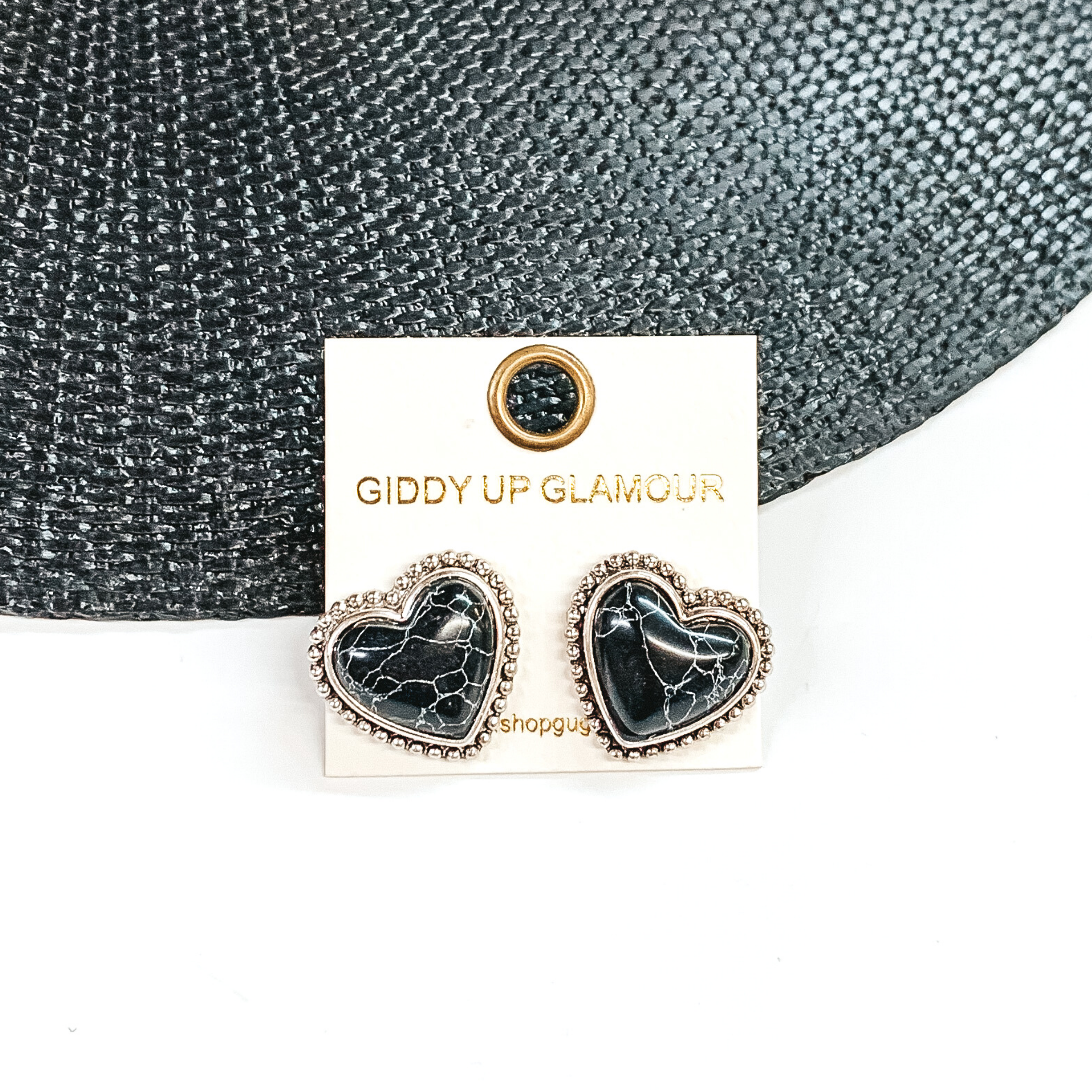 Black, heart stone earrings with a silver backing and outline. These earrings are pictured on a white earrings holder. Then pictured on a white and black background. 