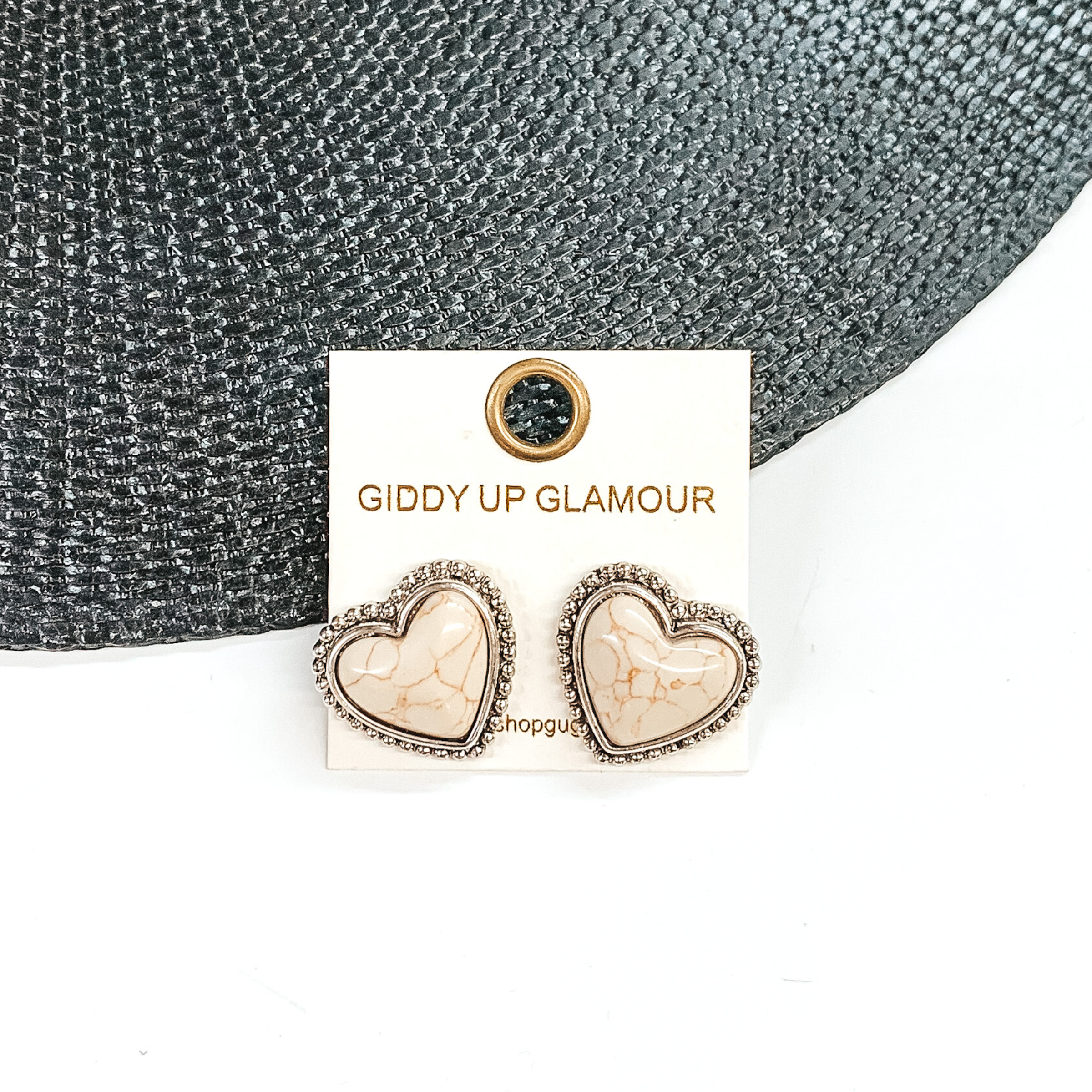 Ivory, heart stone earrings with a silver backing and outline. These earrings are pictured on a white earrings holder. Then pictured on a white and black background.