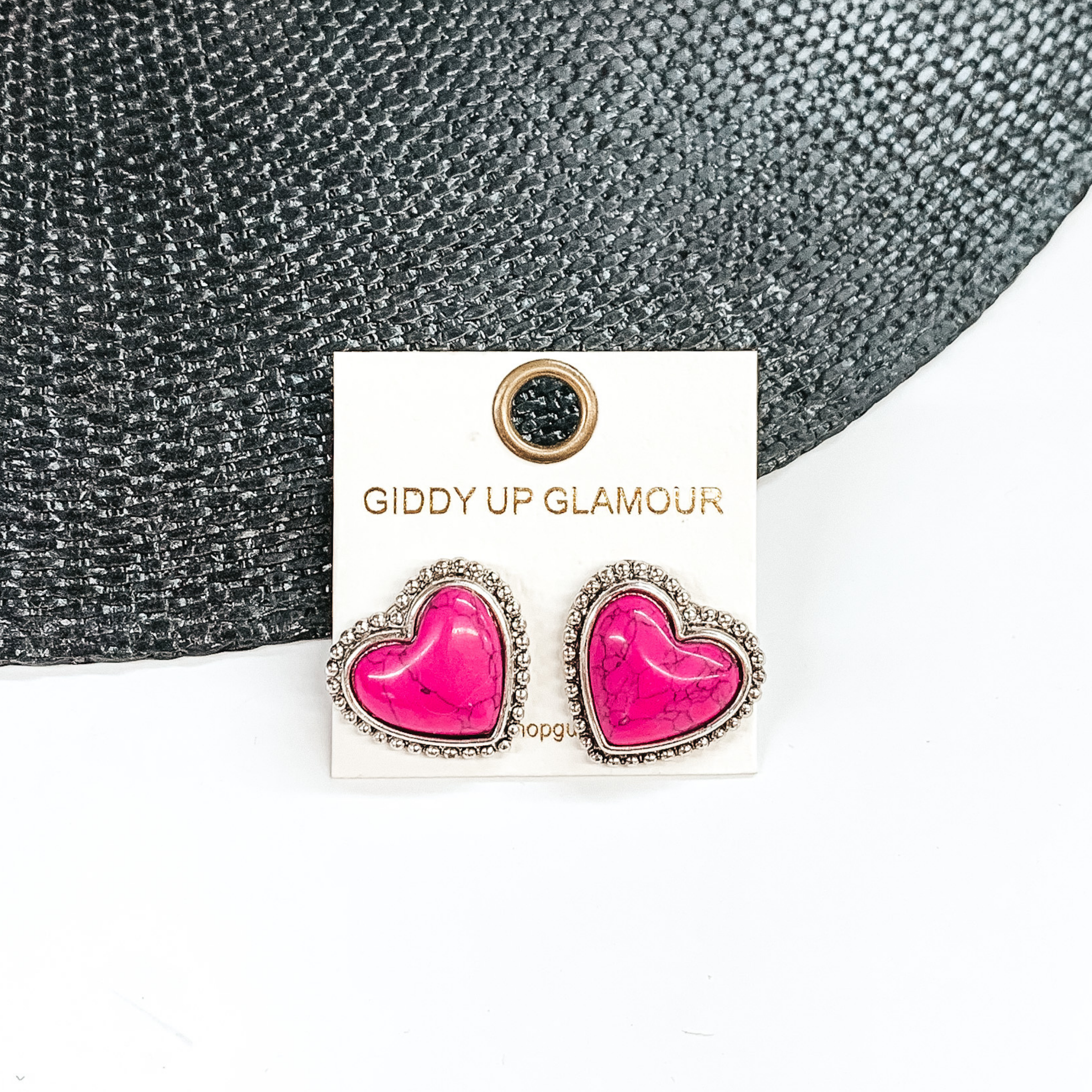 Pink, heart stone earrings with a silver backing and outline. These earrings are pictured on a white earrings holder. Then pictured on a white and black background.