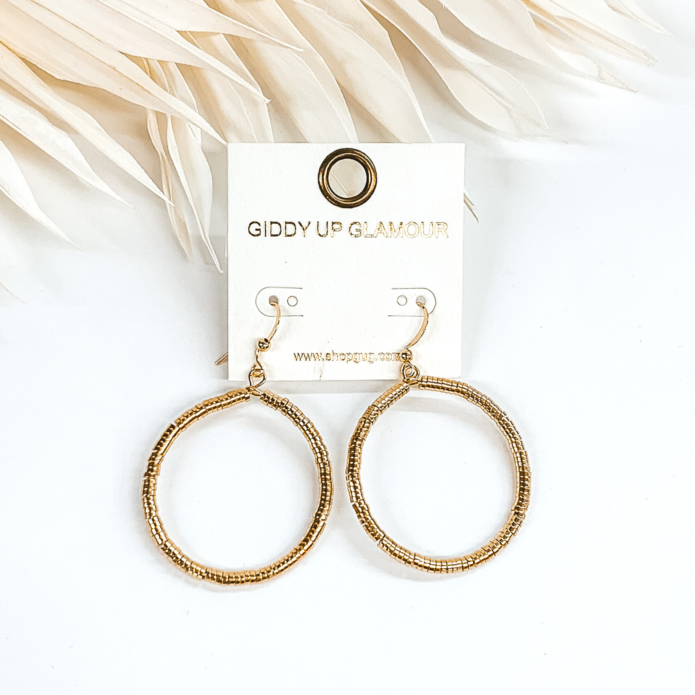Circle drop disk beaded earrings in gold. These earrings are pictured on a white background with ivory leaves at the top of the picture.