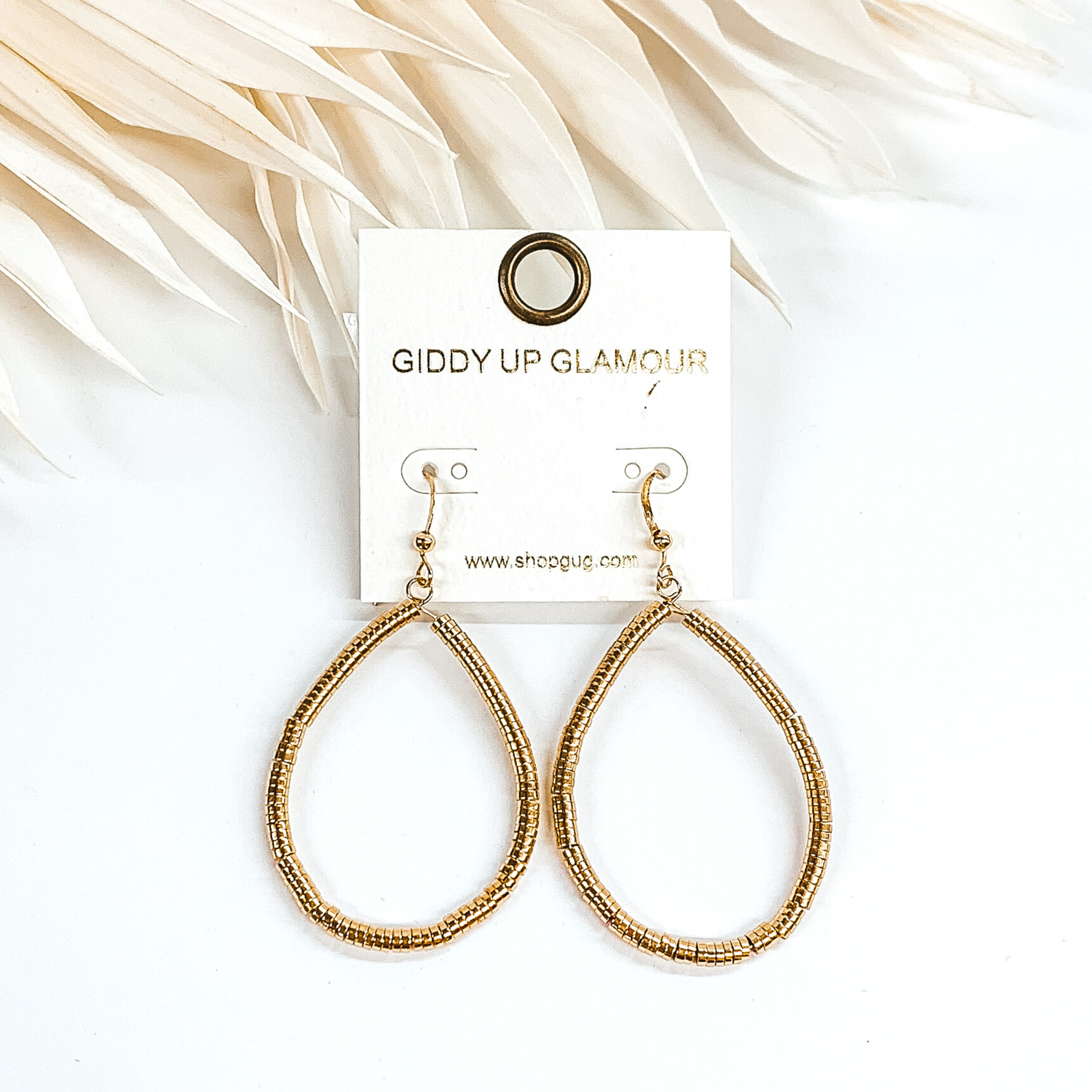 Teardrop disk beaded earrings in gold. These earrings are pictured on a white background with ivory leaves at the top of the picture.