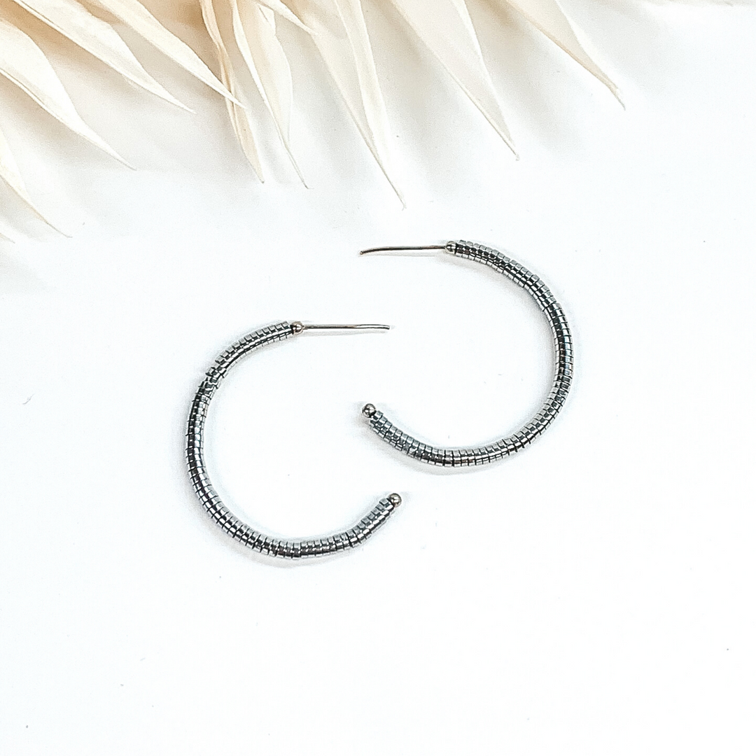  Disk beaded hoop earrings in silver. These earrings are pictured on a white background with ivory leaves at the top of the picture.
