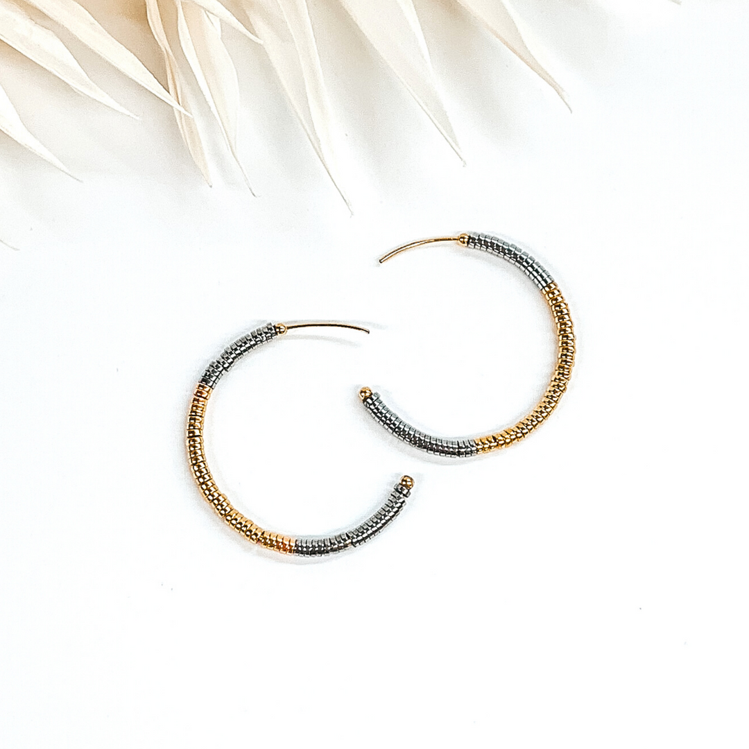 Disk beaded hoop earrings in gold and silver. These earrings are pictured on a white background with ivory leaves at the top of the picture.