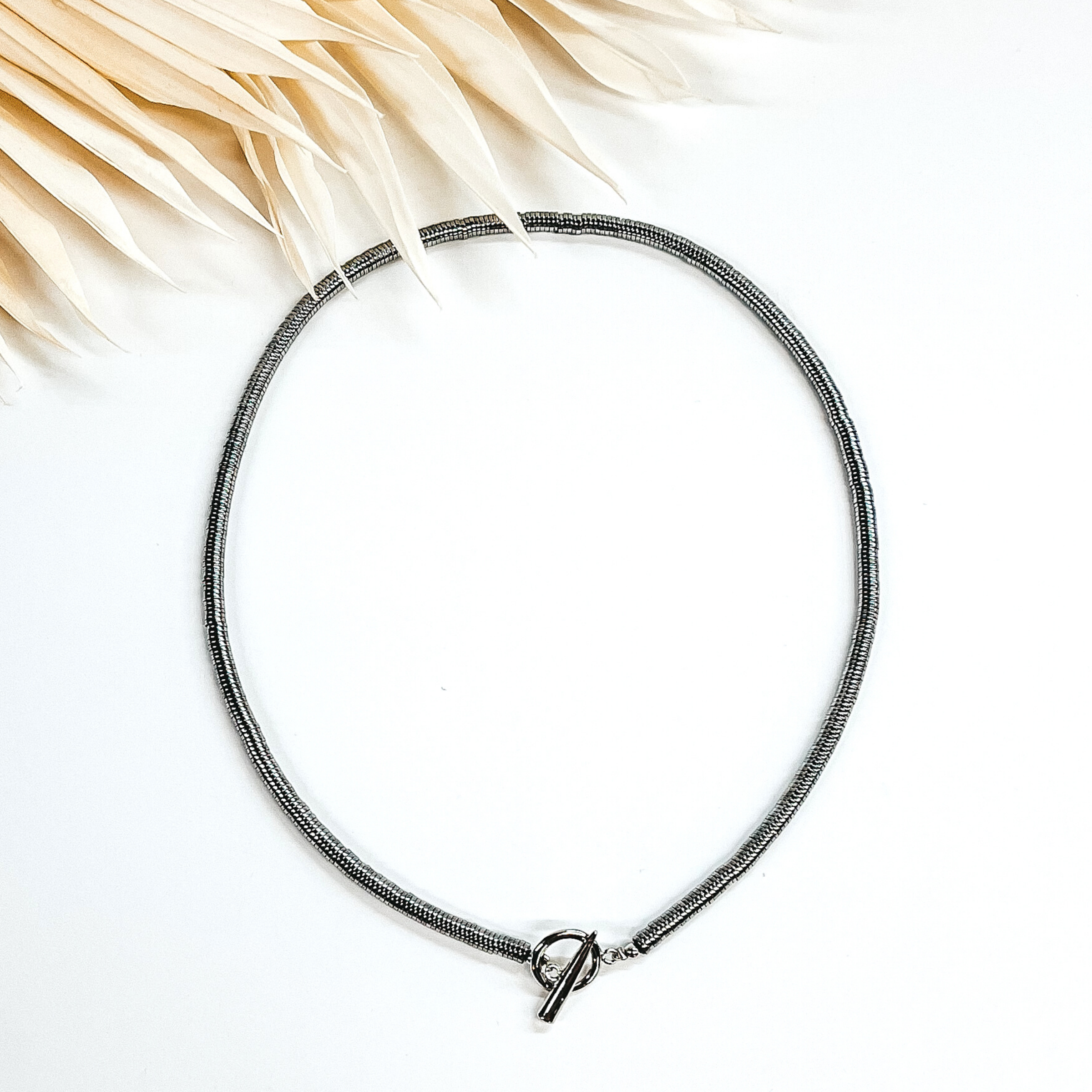 Silver disk beaded necklace with front toggle clasp. This necklace is pictured on a white background with ivory leaves at the top. 