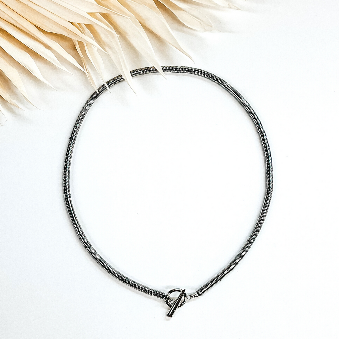 Silver disk beaded necklace with front toggle clasp. This necklace is pictured on a white background with ivory leaves at the top. 