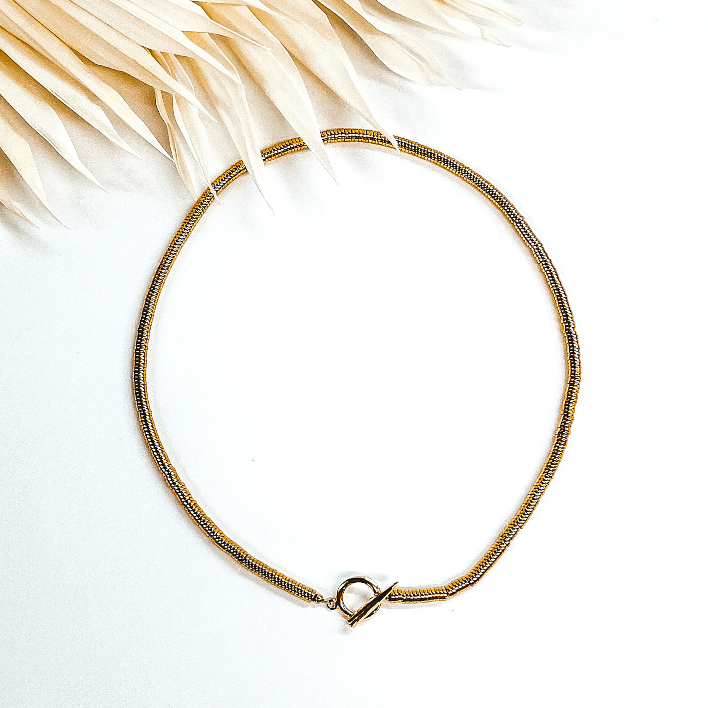 Gold disk beaded necklace with front toggle clasp. This necklace is pictured on a white background with ivory leaves at the top.