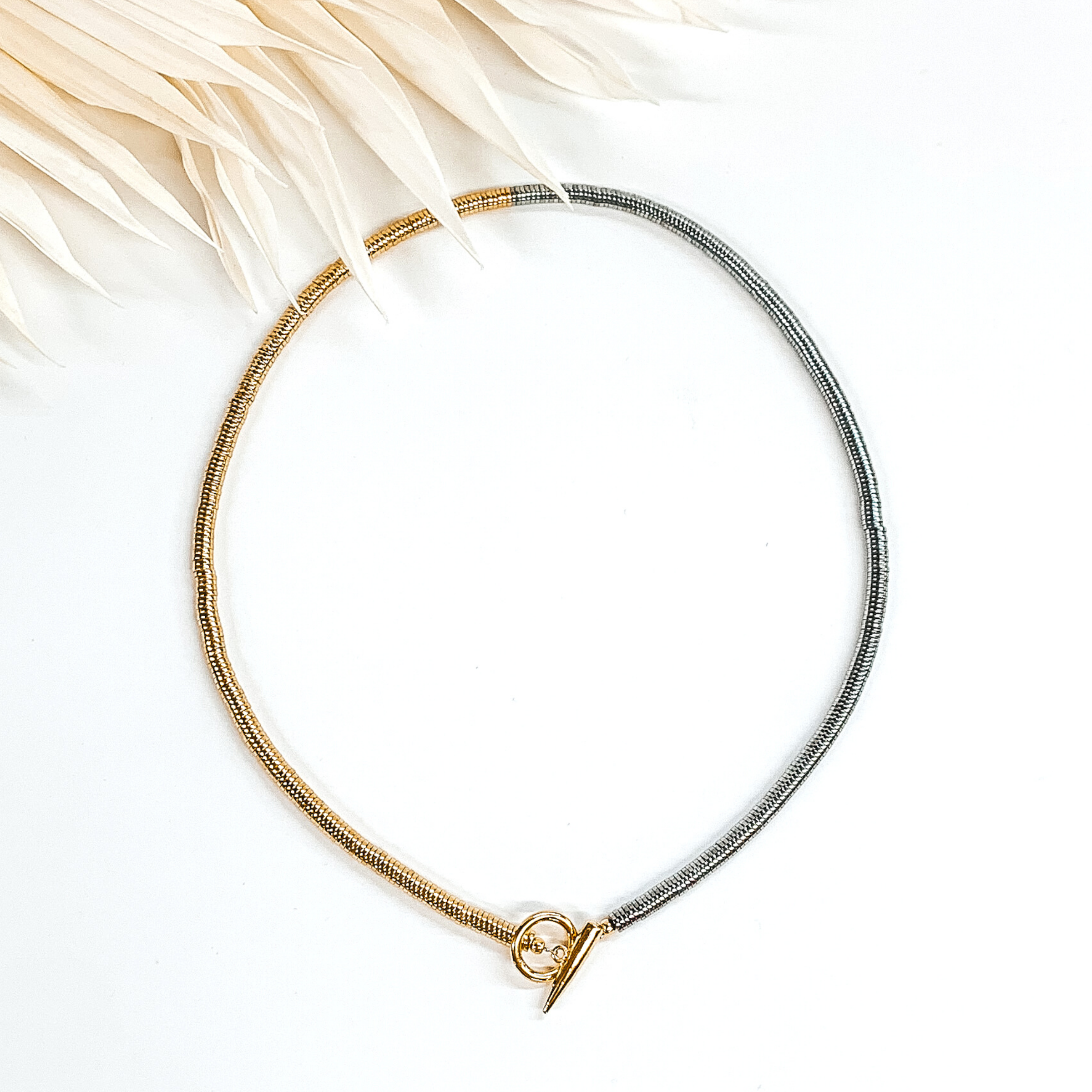 Gold and silver disk beaded necklace with front toggle clasp. This necklace is pictured on a white background with ivory leaves at the top.