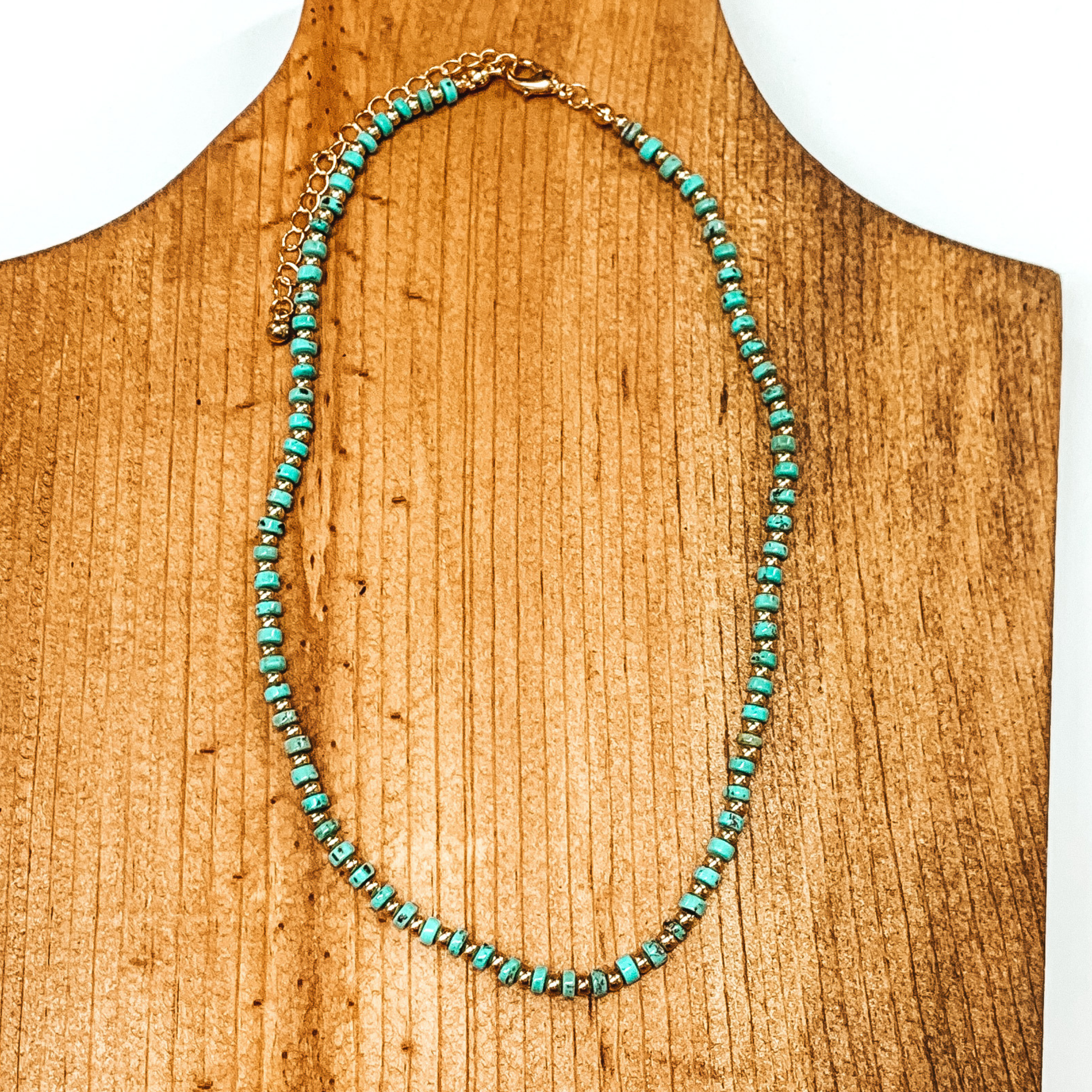 Slab turquoise beads mixed with gold beads necklace. This necklace is pictured on a brown necklace holder on a white background. 
