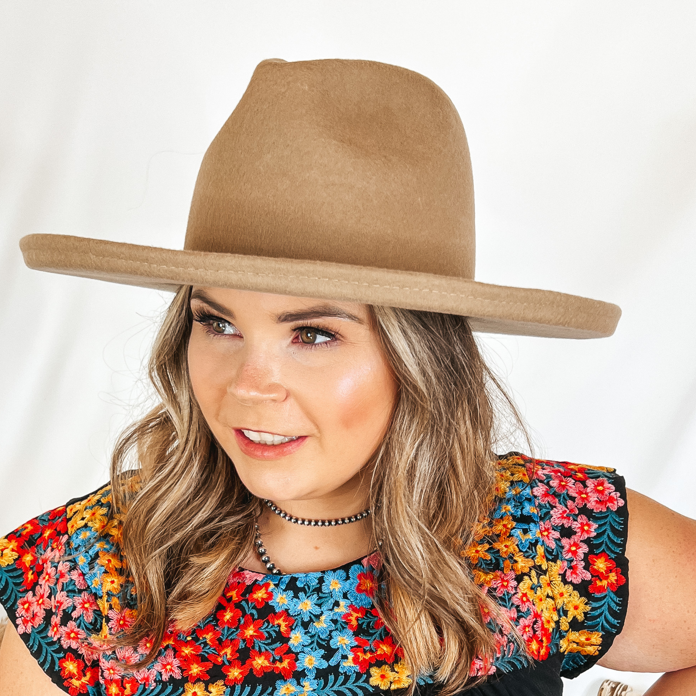 Model is wearing an tan rancher hat with a flat brim with rolled edges.