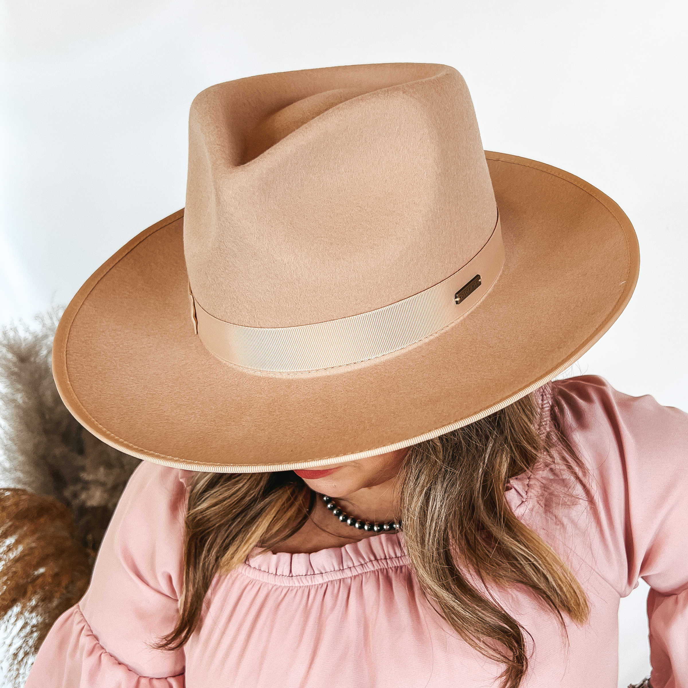 Model is wearing a beige rancher hat with a curved brim.
