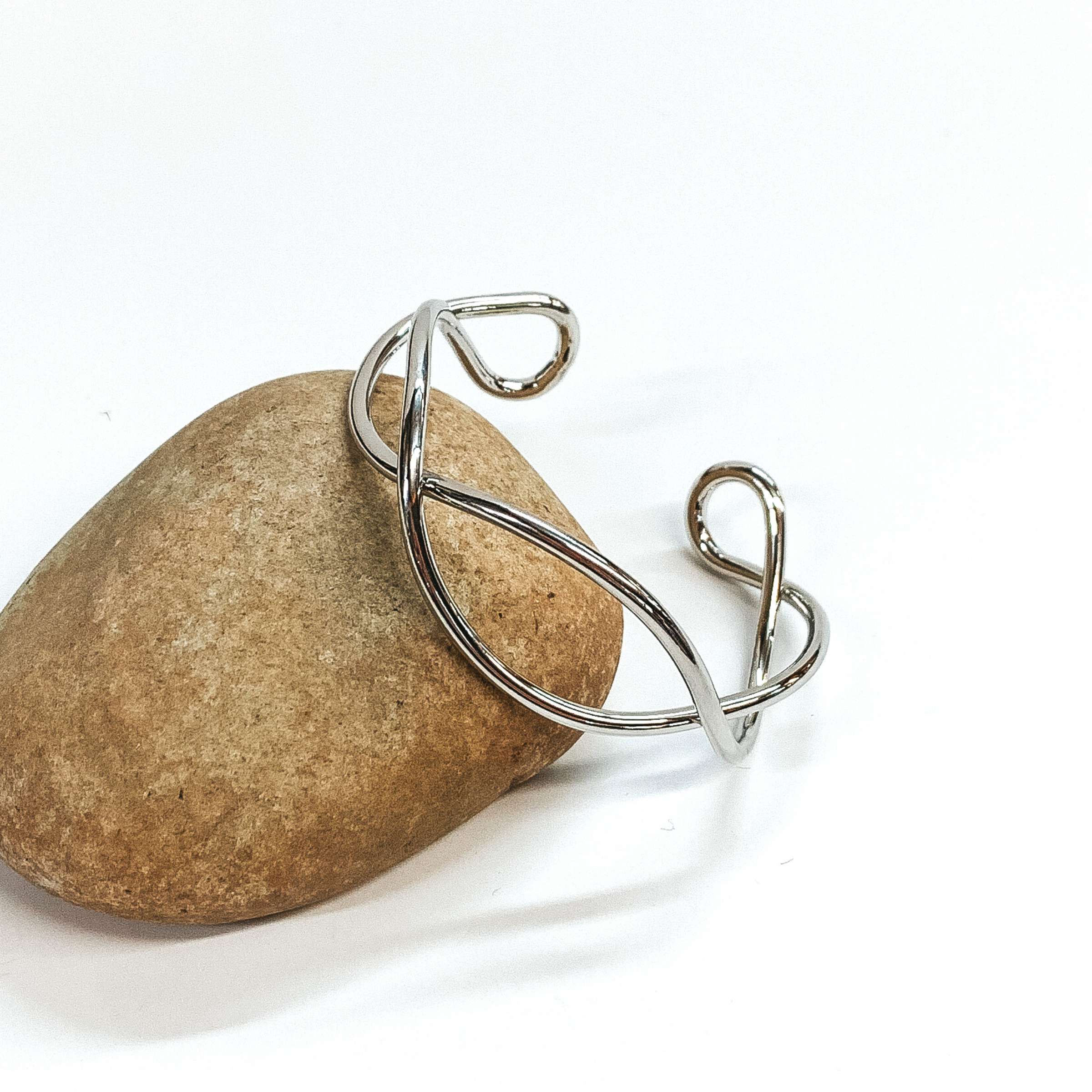 Silver twisted bangle that is pictured leaning against a rock on a white background. 