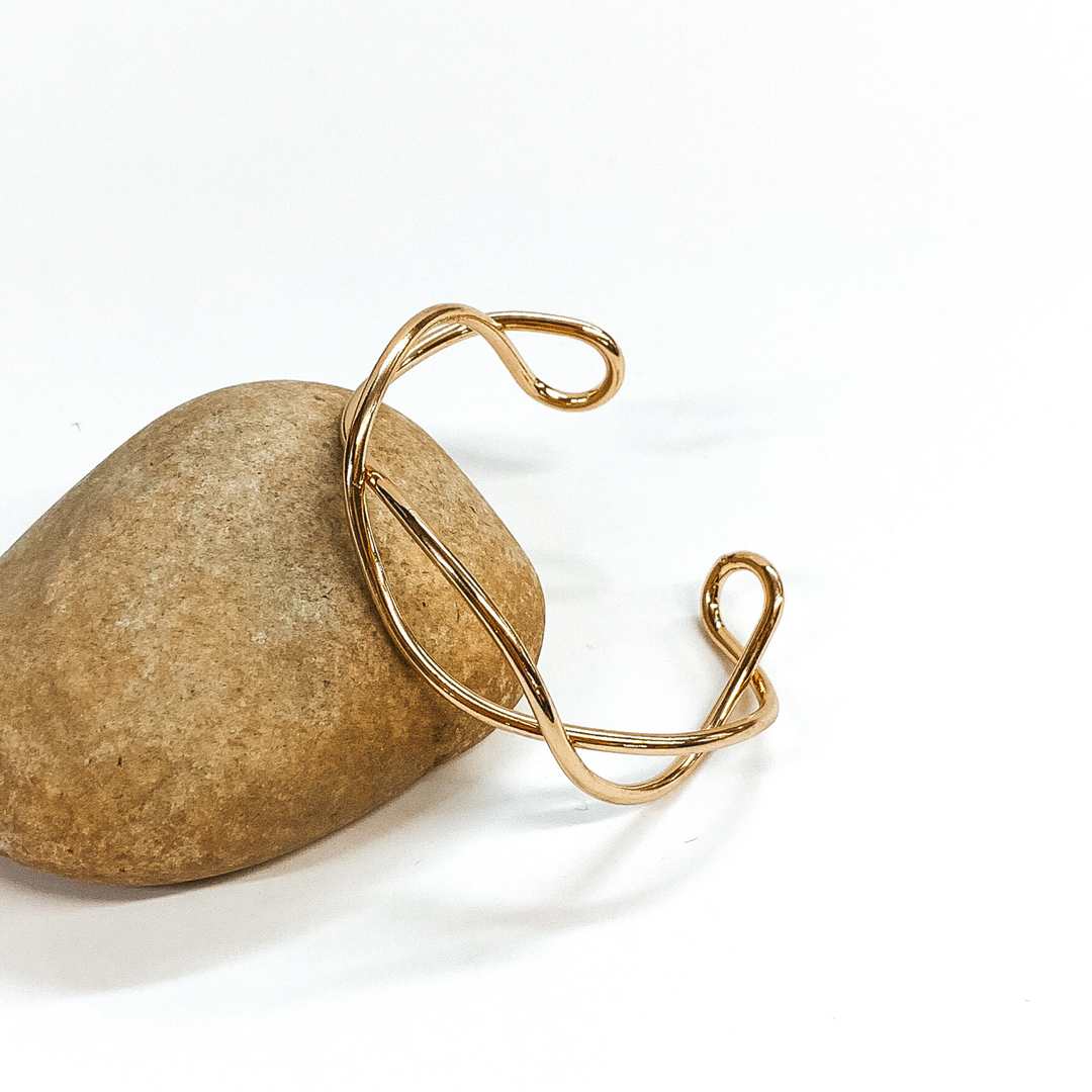 Gold twisted bangle that is pictured leaning against a rock on a white background.