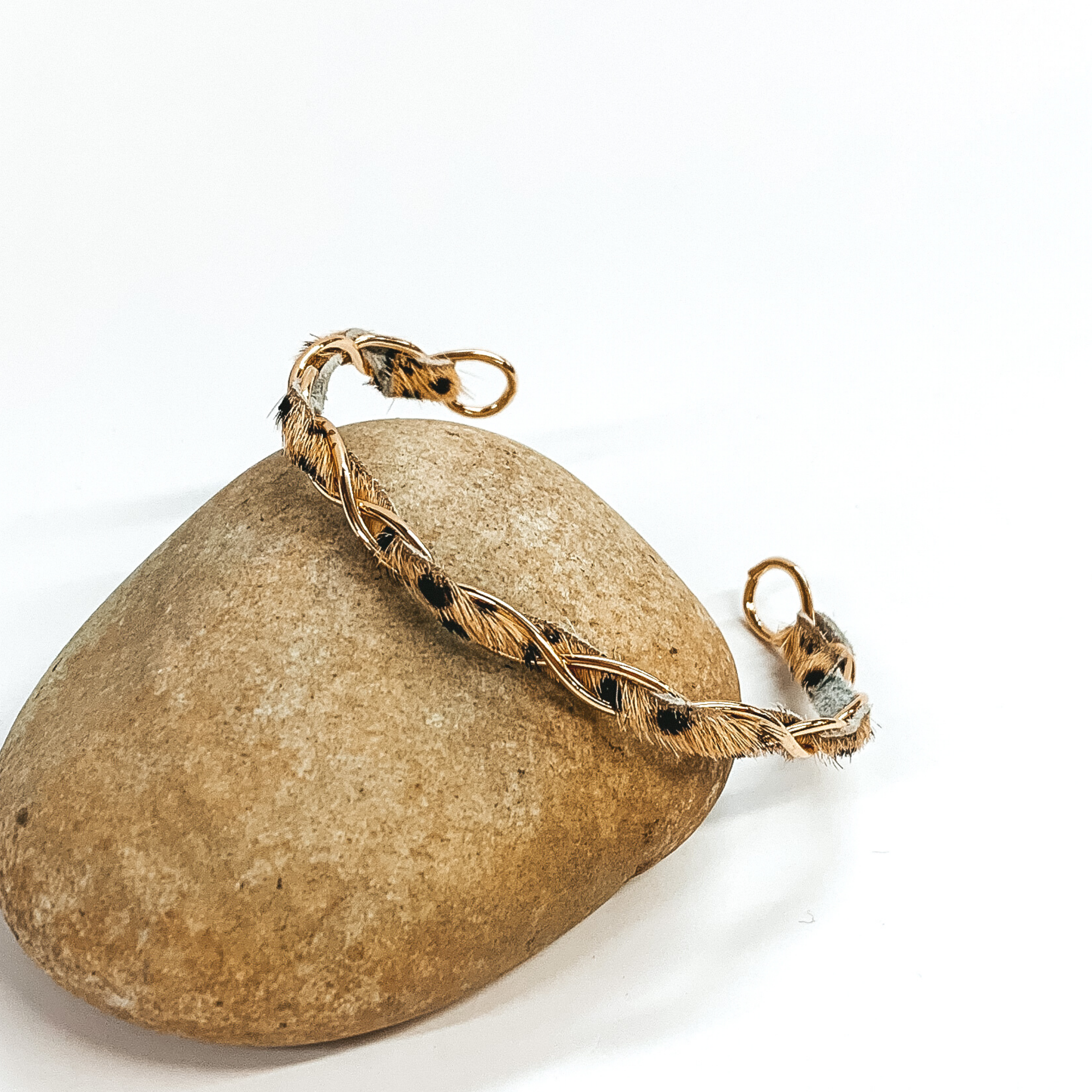 Gold twisted wire bracelet with faux fur inlay in a tan dalmatian print. This bracelet is pictured laying against a rock on a white background.