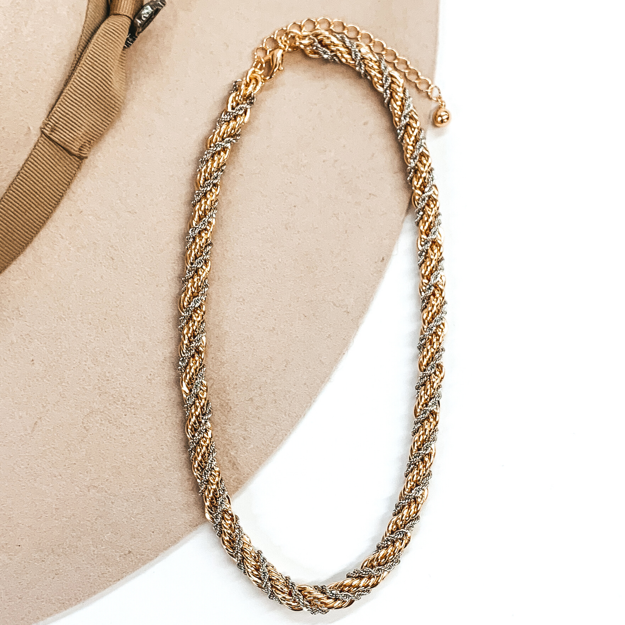 Double twisted rope chained necklace. This necklace includes a gold strand and a silver strand. This necklace is pictured laying in a beige colored hat on a white background. 