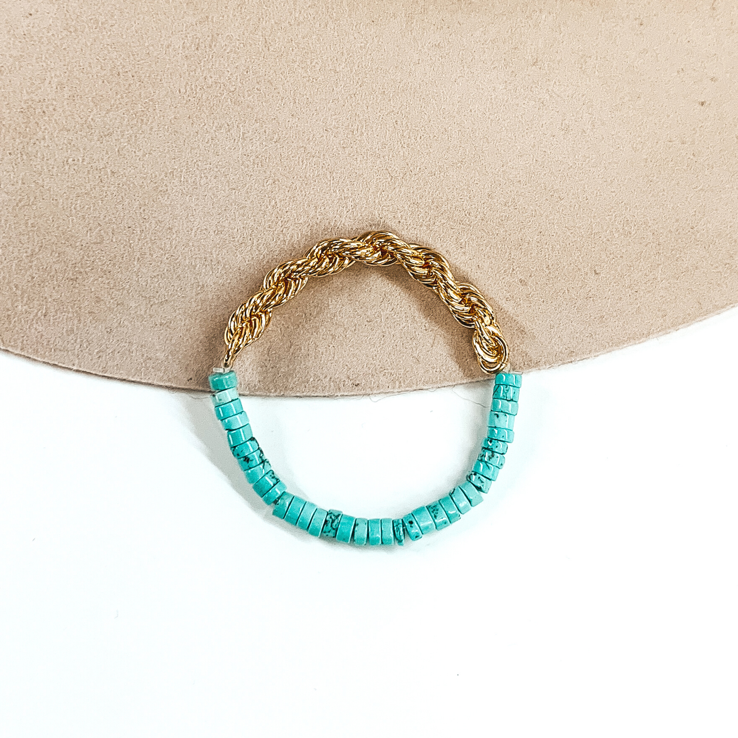 Half of the bracelet is a gold rope chain. While the other half is a turquoise pipestone beaded part. This bracelet is pictured on a white and beige background. 