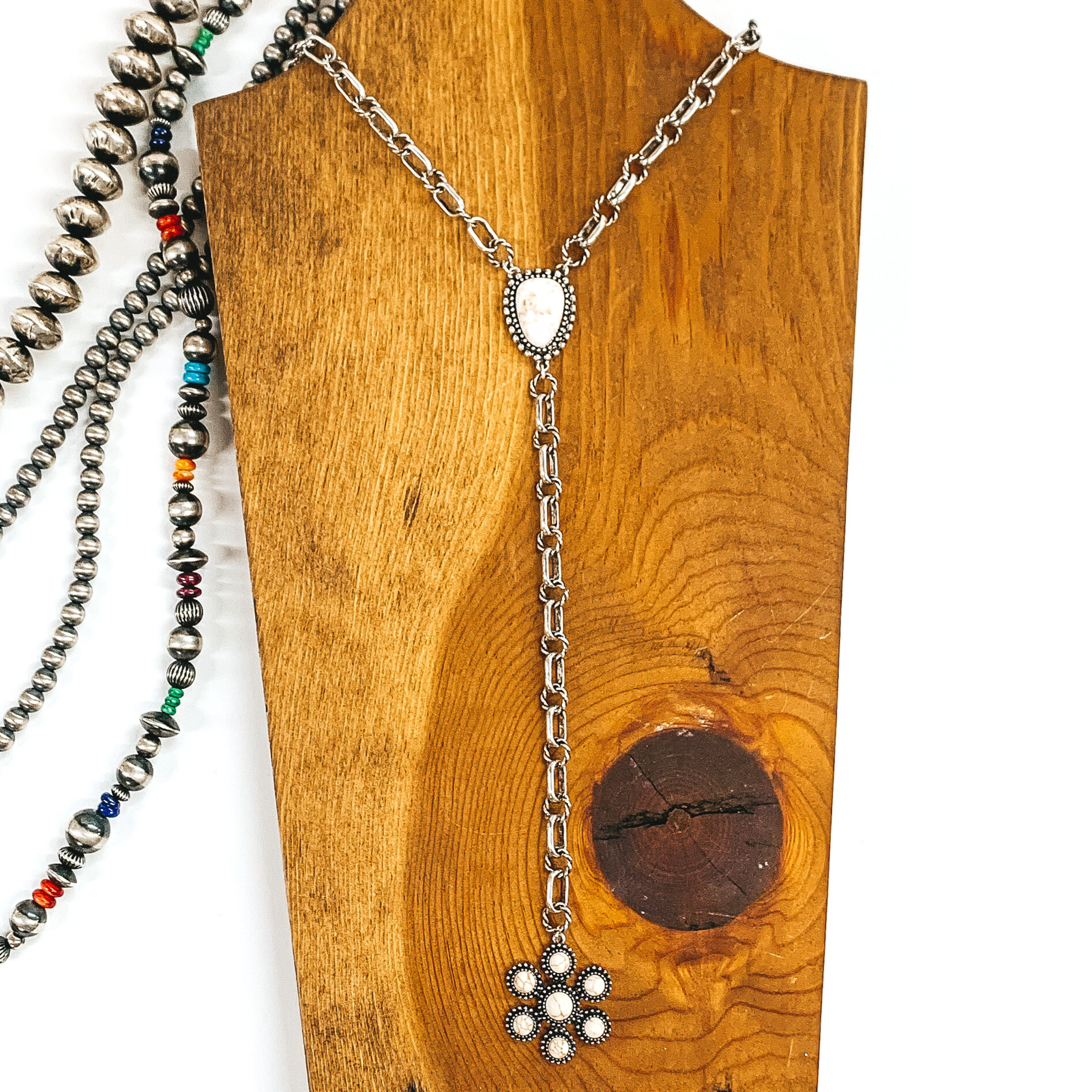 Silver chained necklace that is Navajo inspired with  an ivory irregular stoned pendant. Then hanging from the pendant, there is a hanging silver chain with a star burst pendant with ivory stones. This necklace is pictured on  wood necklace holder on a white background. It has different shaped and colored navajo strands. 
