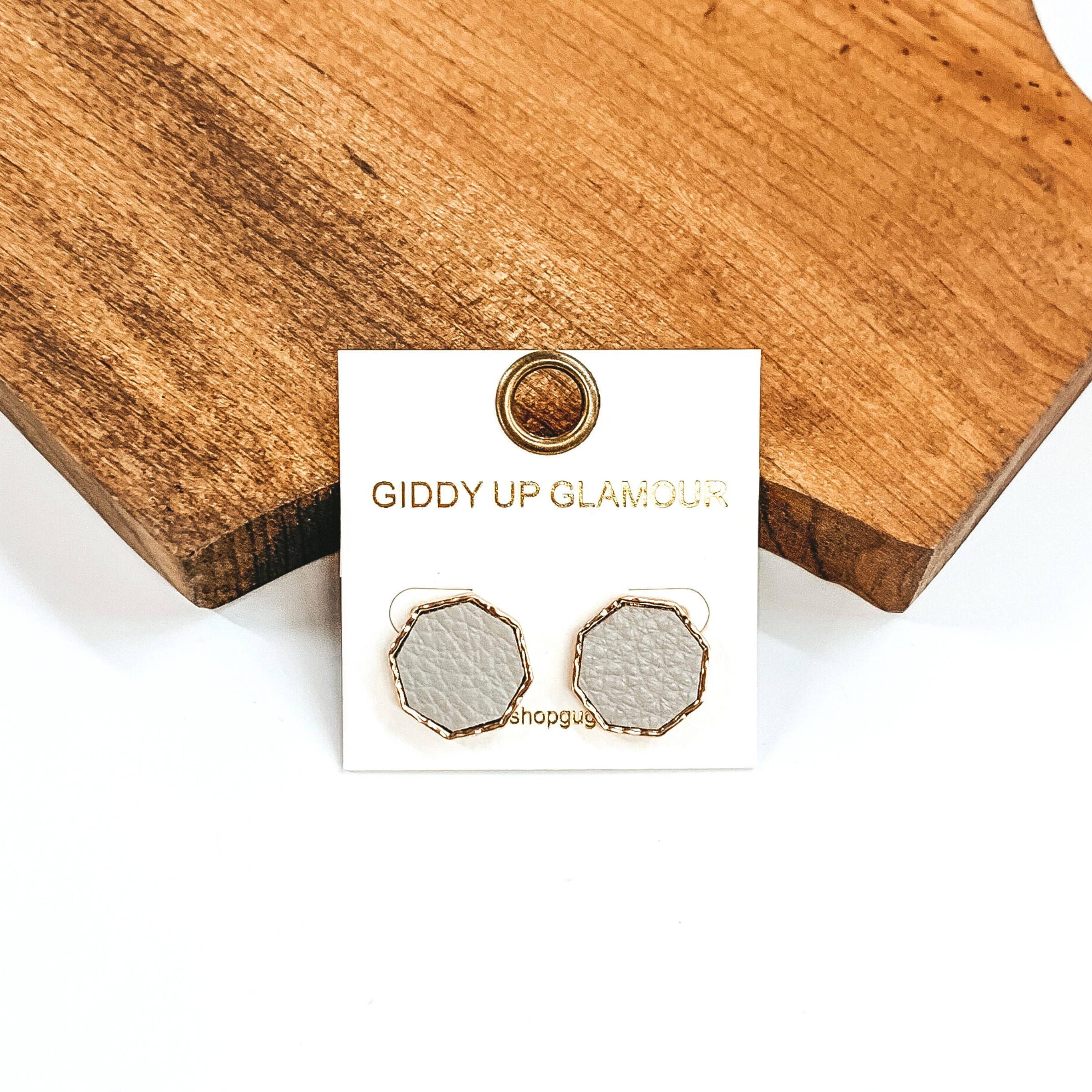 Gold, hexagon stud earrings with an grey leather like inlay. Pictured on a white background in front of a piece of wood.