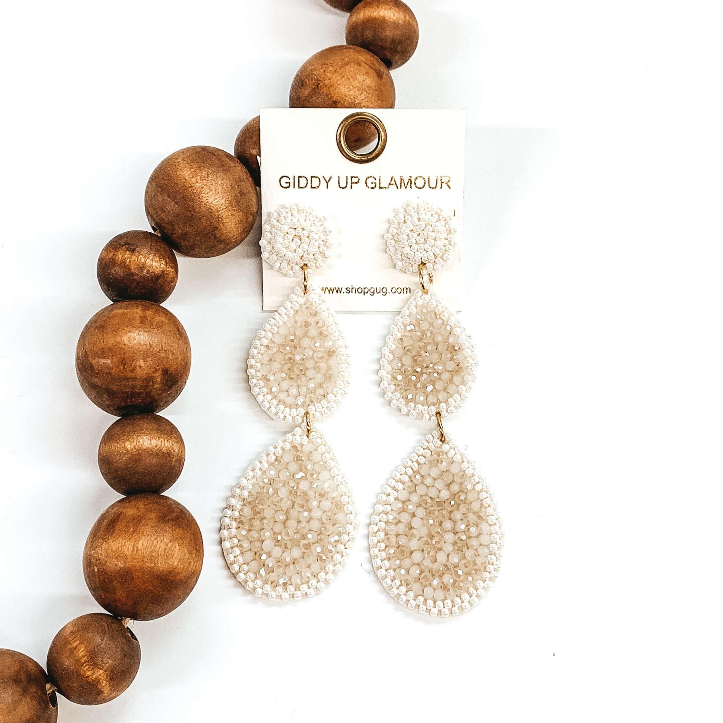 Beaded three tiered earrings in ivory. These earrings start off with a circle then has two hanging teardrops with both increasing in size as they go down. These earrings are pictured on a white background with dark brown beads on the left side of the earrings.