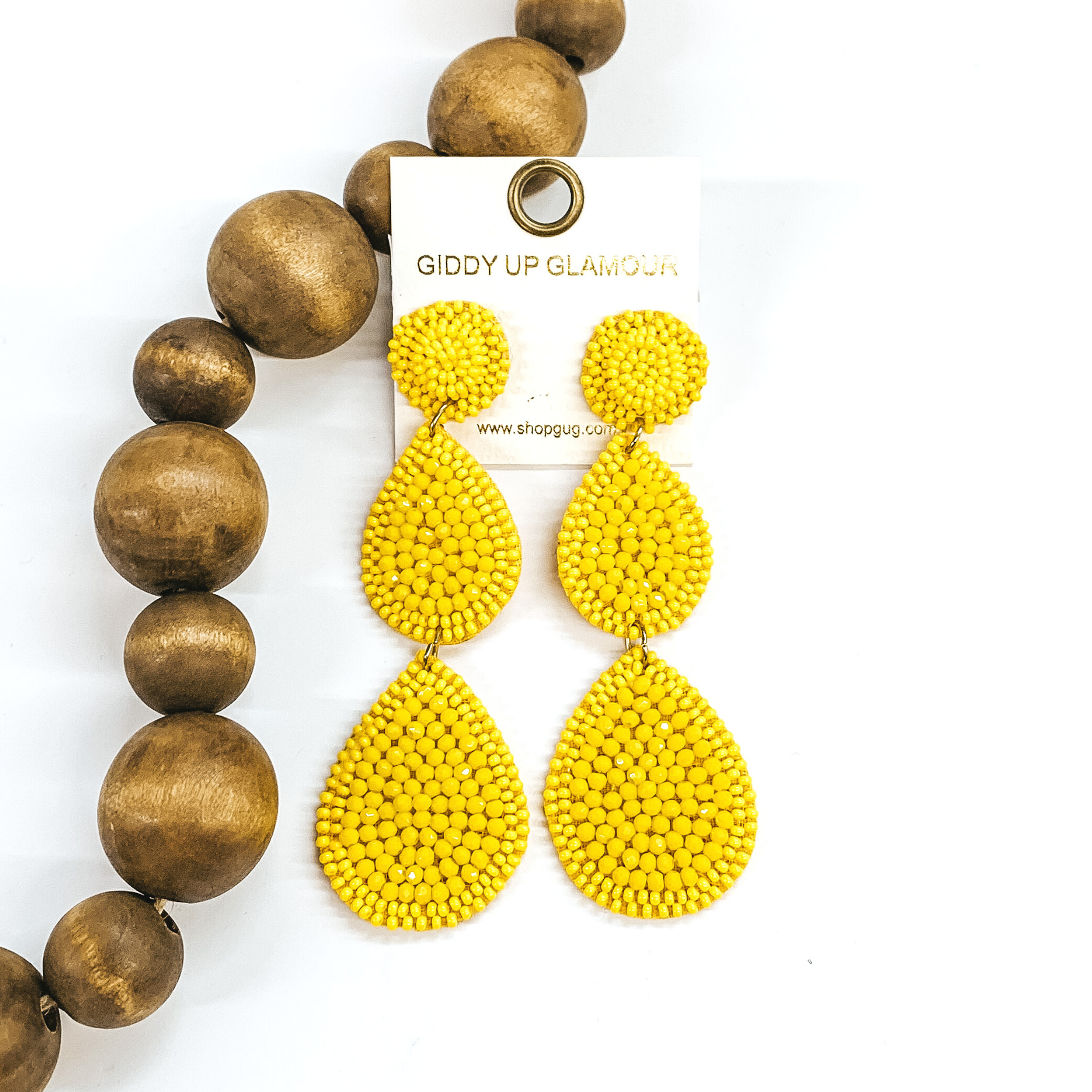 Beaded three tiered earrings in yellow. These earrings start off with a circle then has two hanging teardrops with both increasing in size as they go down. These earrings are pictured on a white background with dark brown beads on the left side of the earrings.