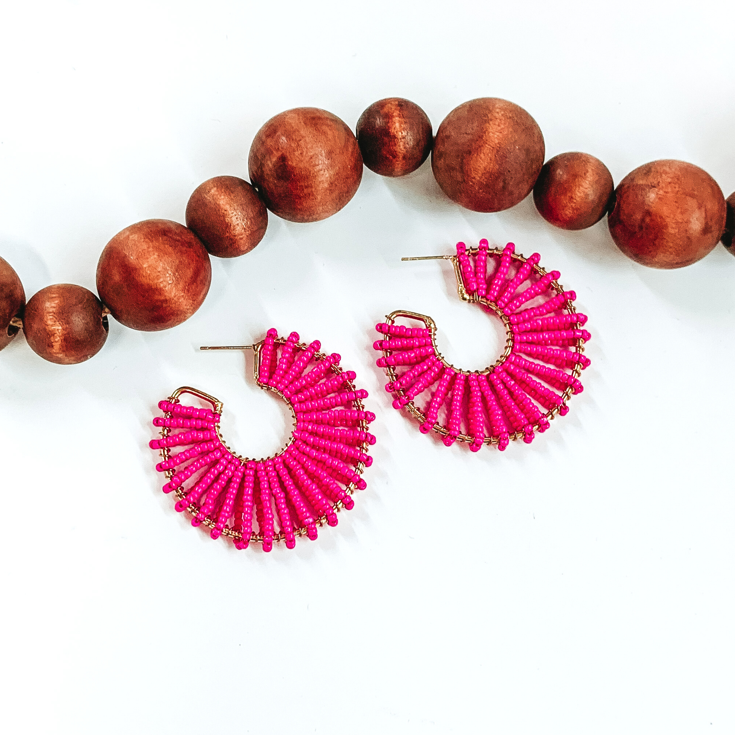 Gold outlined, thick hoops. Wrapped around the gold outline are a hot pink beaded string. These earrings are pictured on a white background with dark brown beads at the top of the picture. 