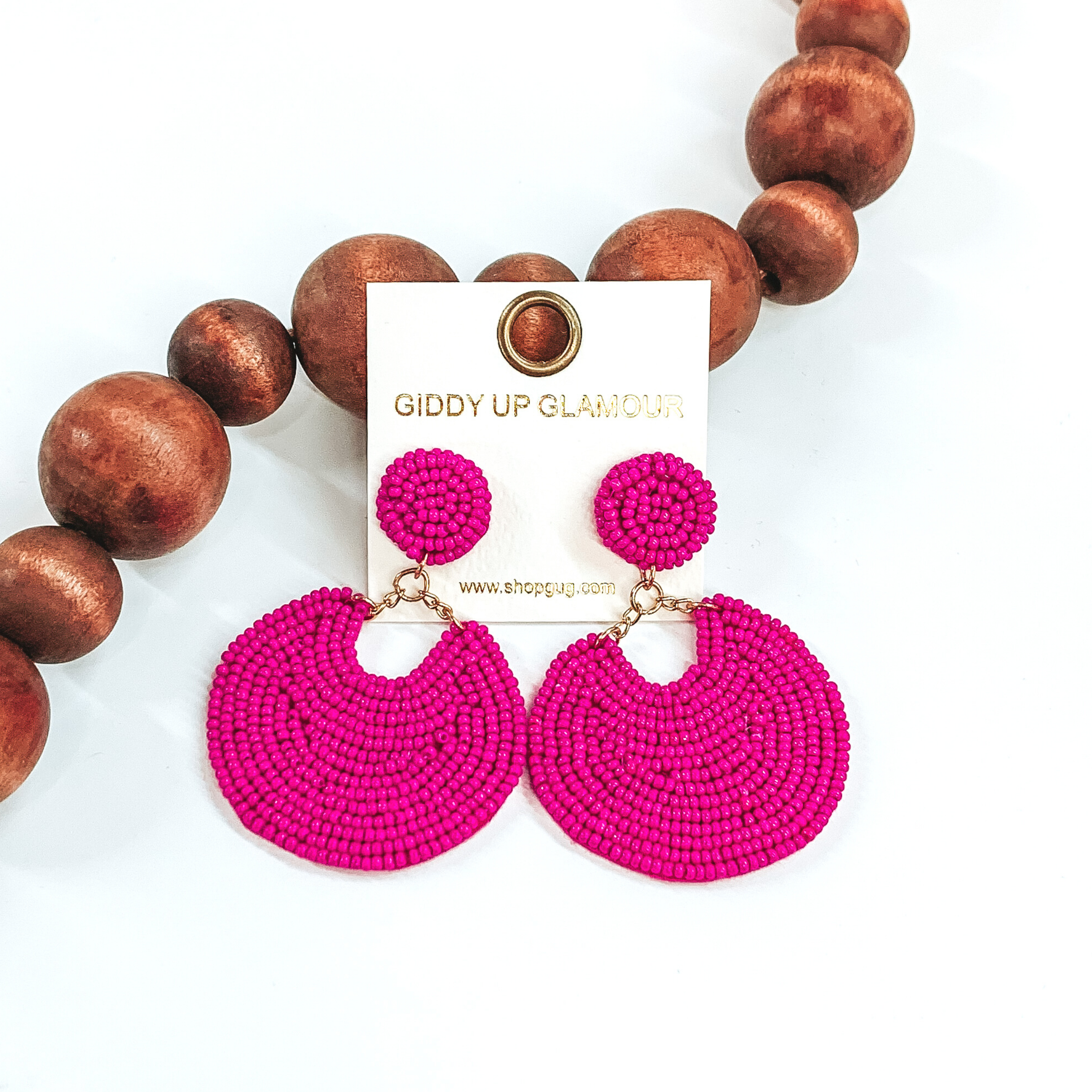 Beaded circle studs with a hanging bigger circle with a small "u" cutout. These beaded earrings in the the color fuchsia. These earrings are pictured on a white background with dark brown beads on the left side of the earrings.