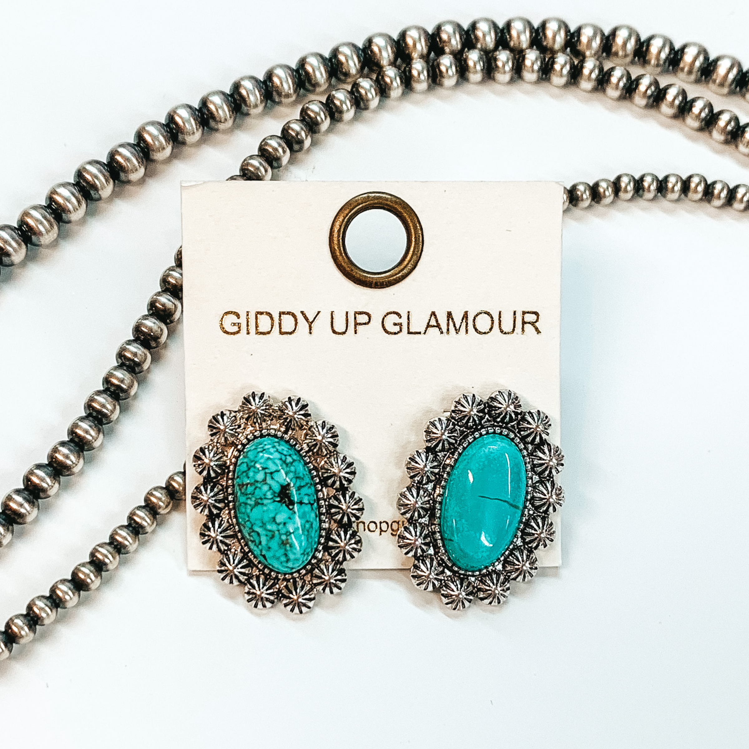 Shown here are post back earrings with a turquoise stone in the center with silver lining with engraved details. Taken in a white background with beads as decor.