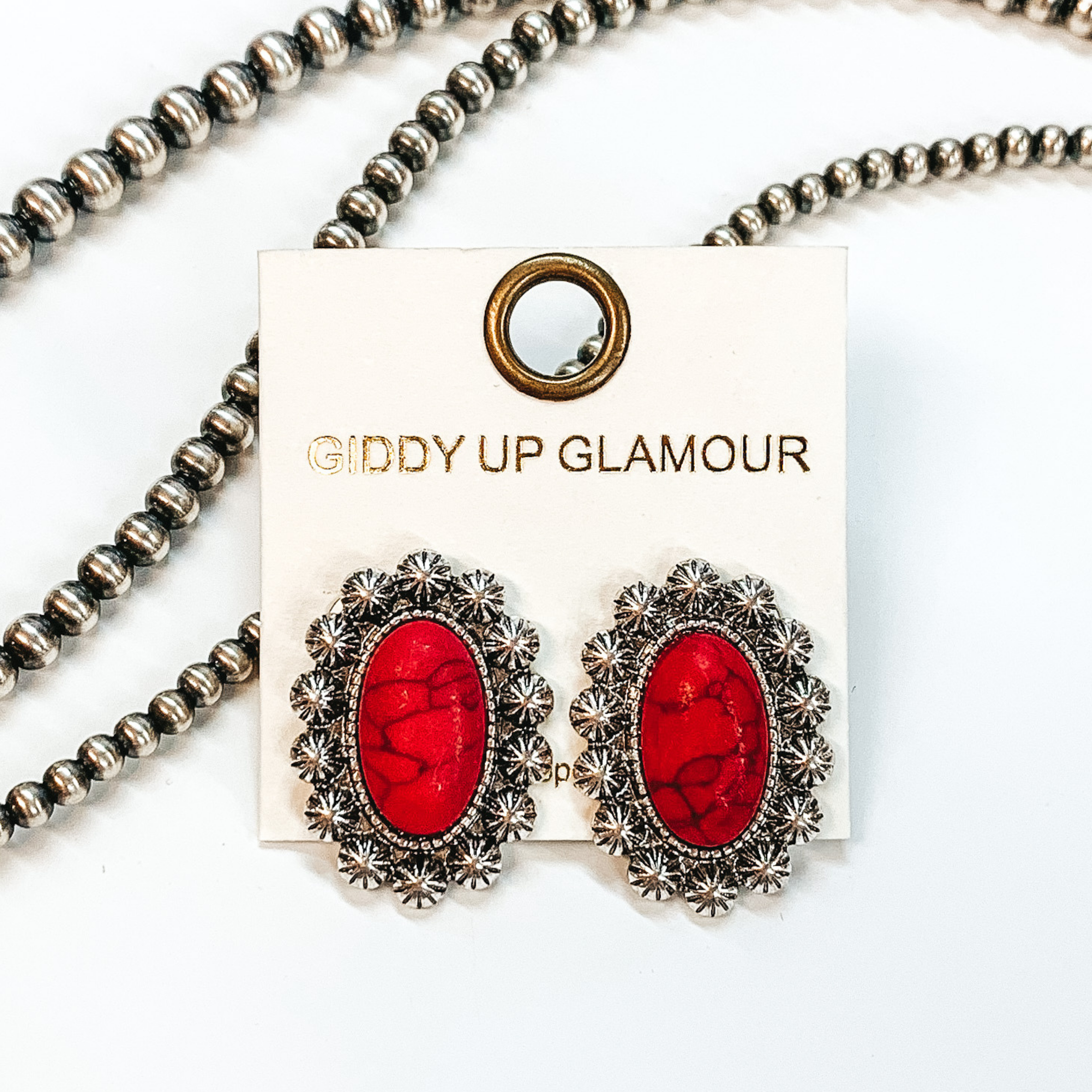Shown here are post back earrings with a red stone in the center with silver lining with  engraved details. Taken in a white background with  beads as decor.